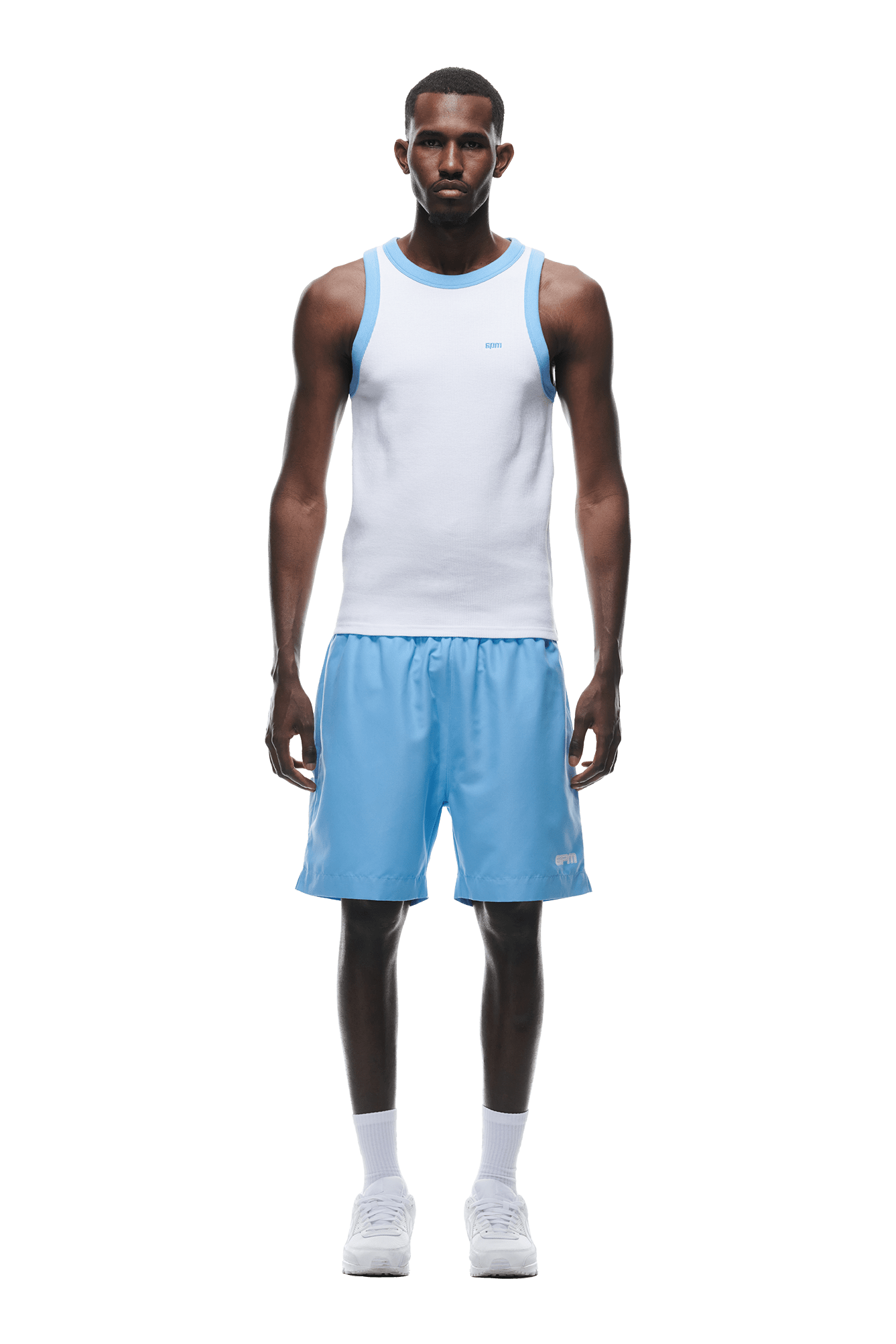 A man stands facing forward in a 6PM WAFFLE KNIT TANKTOP WHITE, light blue athletic shorts, white crew socks, and white sneakers against a plain white background.