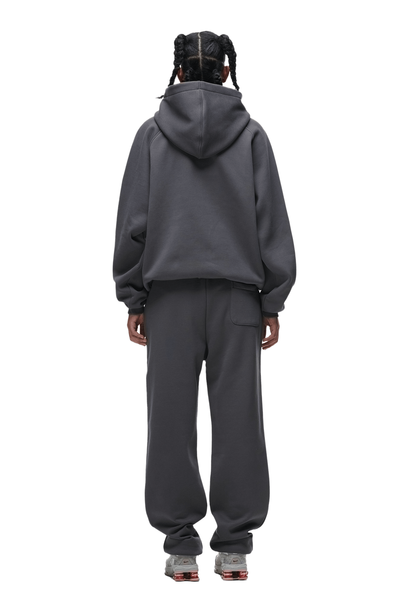 A person with braided hair faces away, wearing the 6PM HOODIE ANTHRACITE and matching sweatpants with gray sneakers against a solid green background.