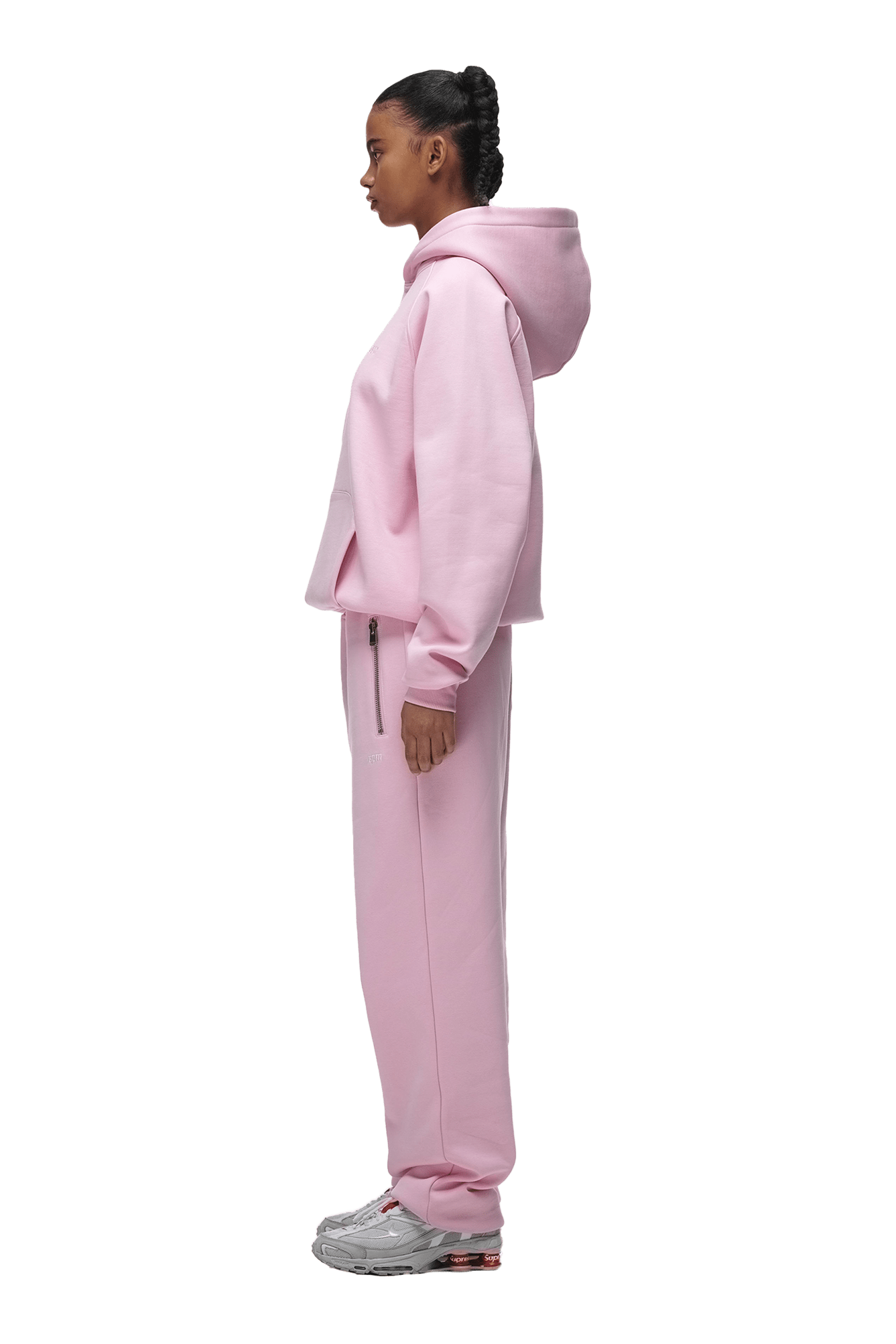A person stands in profile wearing the 6PM HOODIE BABY PINK with matching pink sweatpants and gray sneakers, shown against a transparent background—ideal for everyday wear.