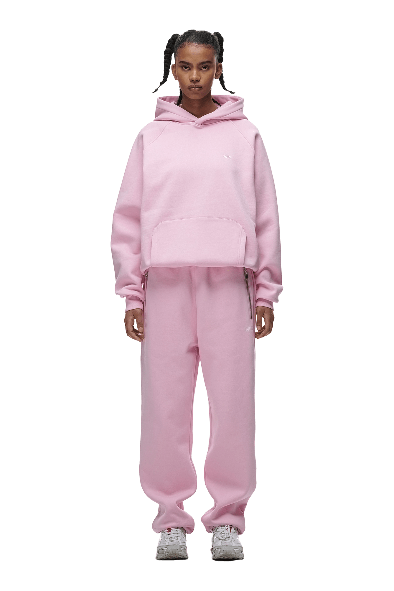 A person faces forward in a 6PM HOODIE BABY PINK with matching sweatpants and silver sneakers. Their hair is styled in braided pigtails. The background is transparent.