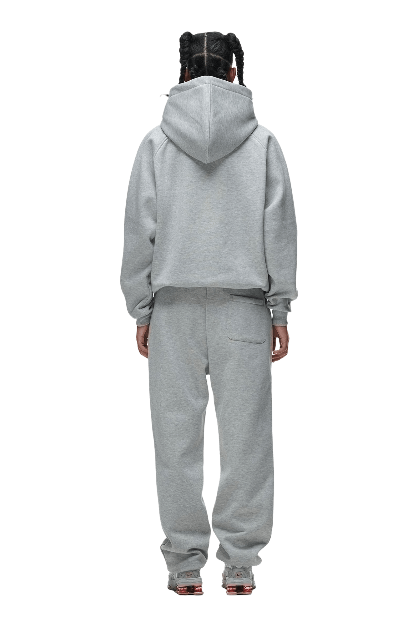 A person stands with their back to the camera, hands by their sides, hair in multiple braids, wearing the 6PM HOODIE GREY MELANGE—a light gray raglan-sleeved hoodie and matching sweatpants ideal for everyday wear.