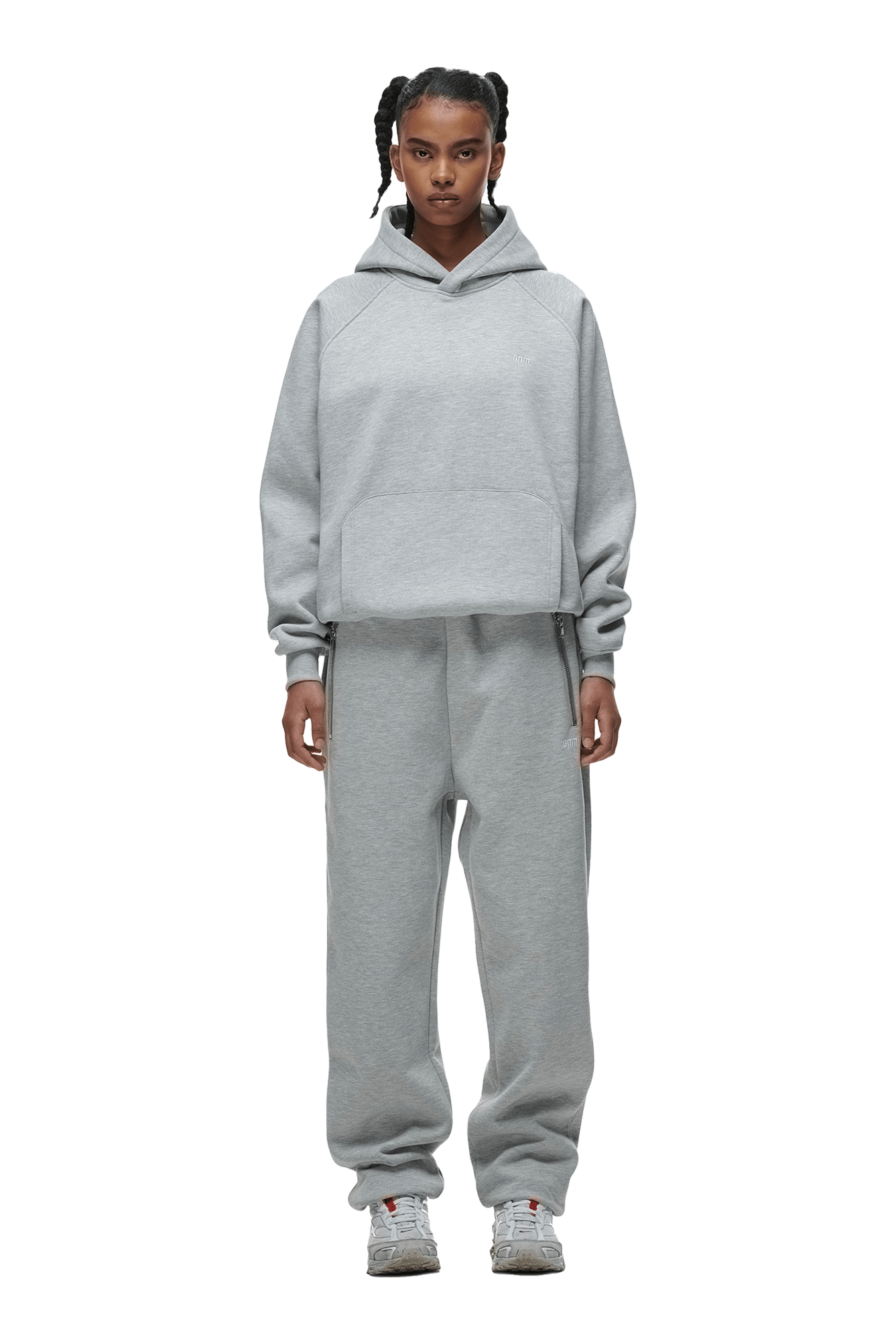 A person faces forward, wearing the 6PM HOODIE GREY MELANGE with matching sweatpants and white sneakers. Their hair is in two braids, and the background is transparent.