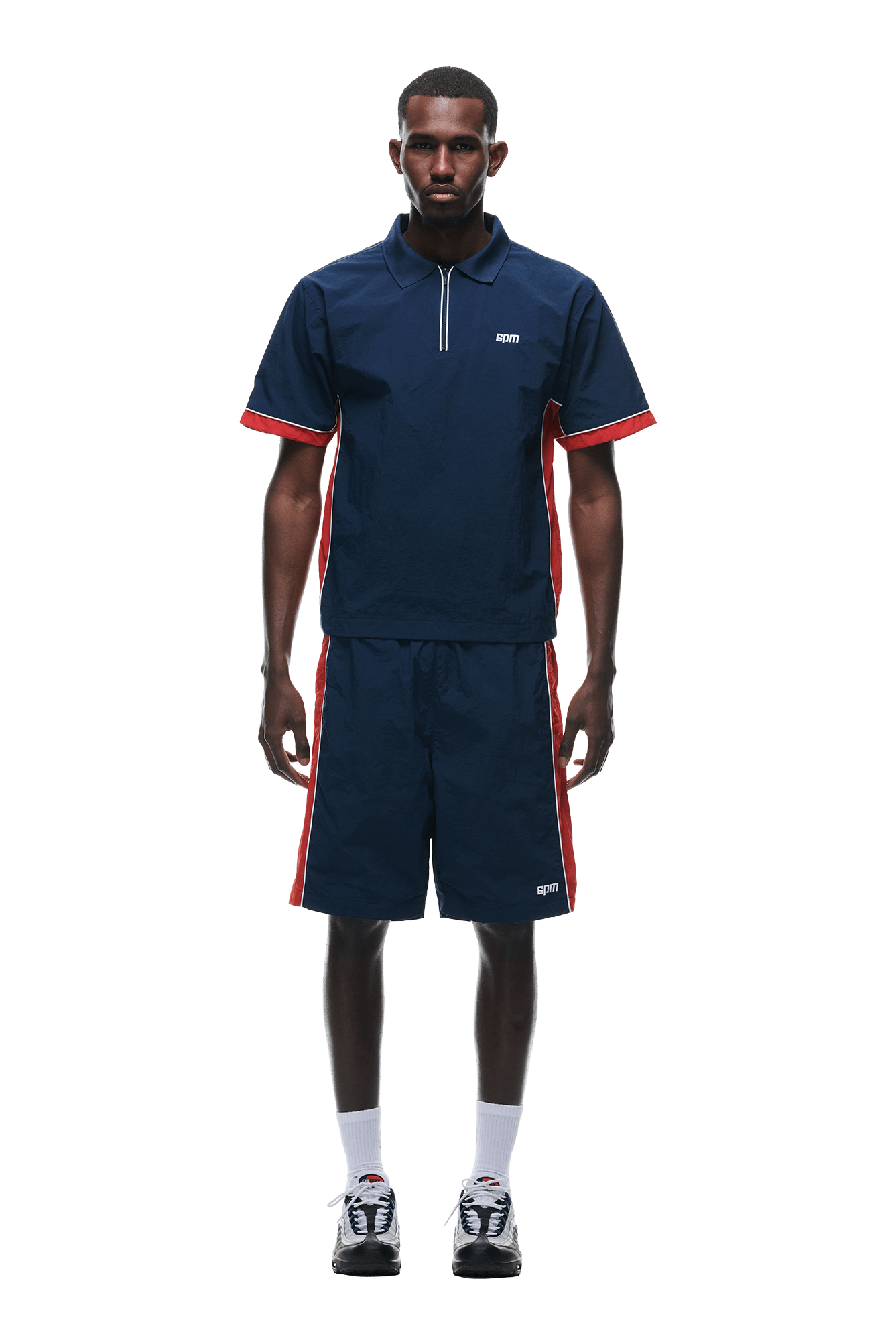 A man faces forward wearing the 6PM WARM UP NYLON HALF ZIP NIGHT SKY shirt and matching shorts with red and white side stripes, paired with white socks and black sneakers, all set against a white background.