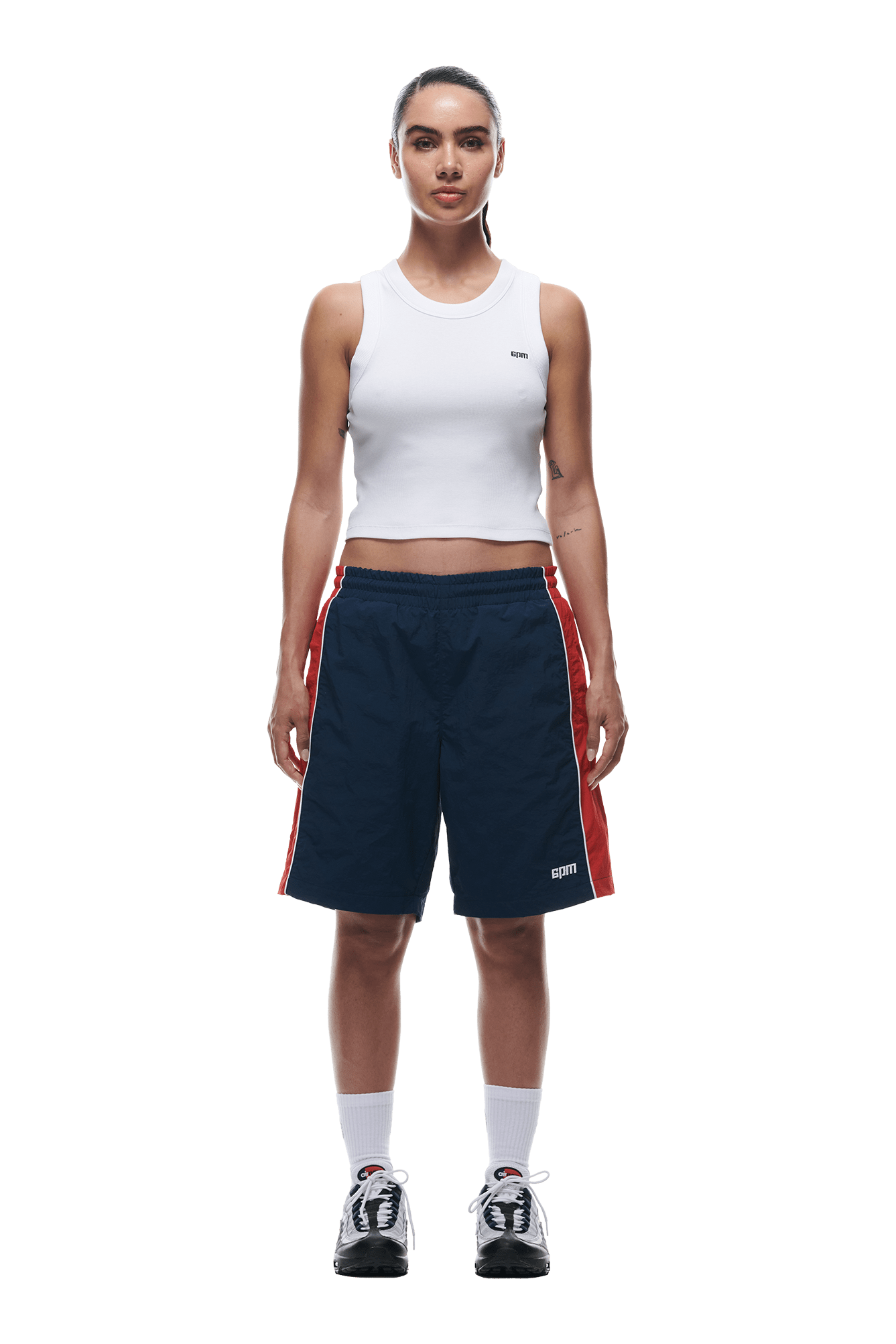 A woman faces forward against a white background, wearing a white sleeveless crop top, 6PM WARM UP NYLON SHORTS NIGHT SKY, white crew socks, and black-and-white sneakers.