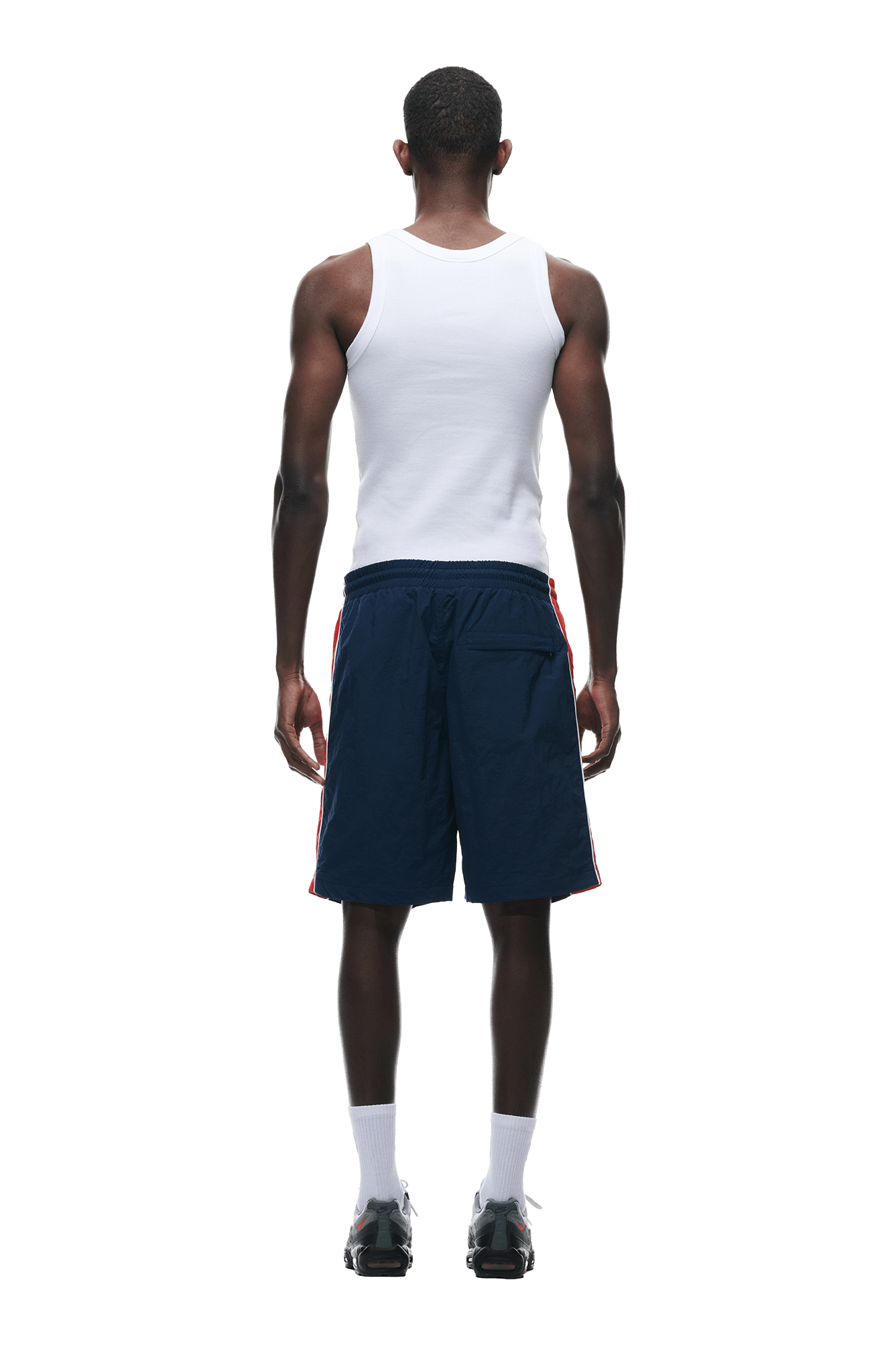 A man faces away from the camera, wearing a white tank top, 6PM WARM UP NYLON SHORTS NIGHT SKY with red side stripes, white socks, and black sneakers against a plain white background.