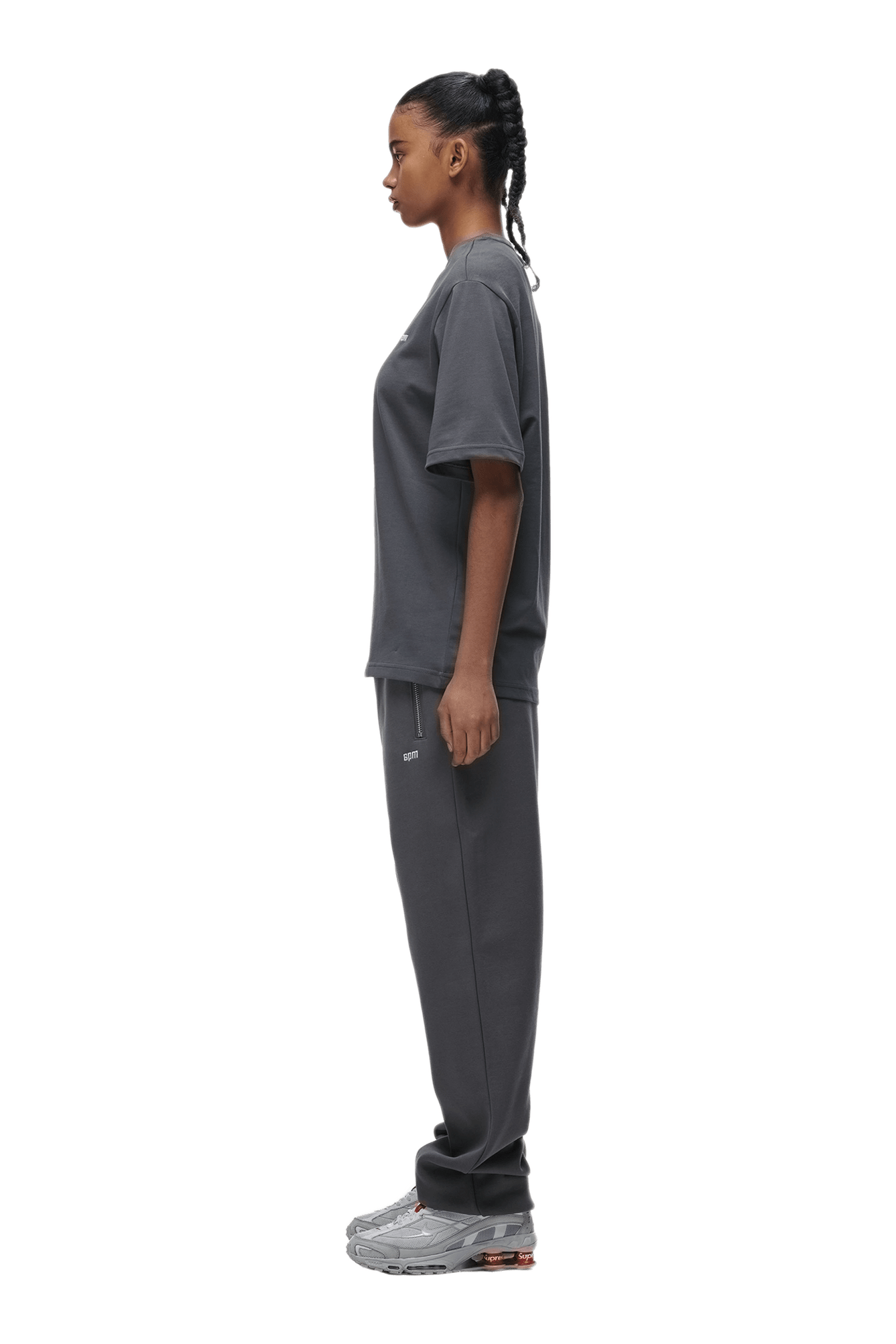 A person in profile, facing left, wears the 6PM T-SHIRT ANTHRACITE with matching sweatpants and gray sneakers. The background is transparent.