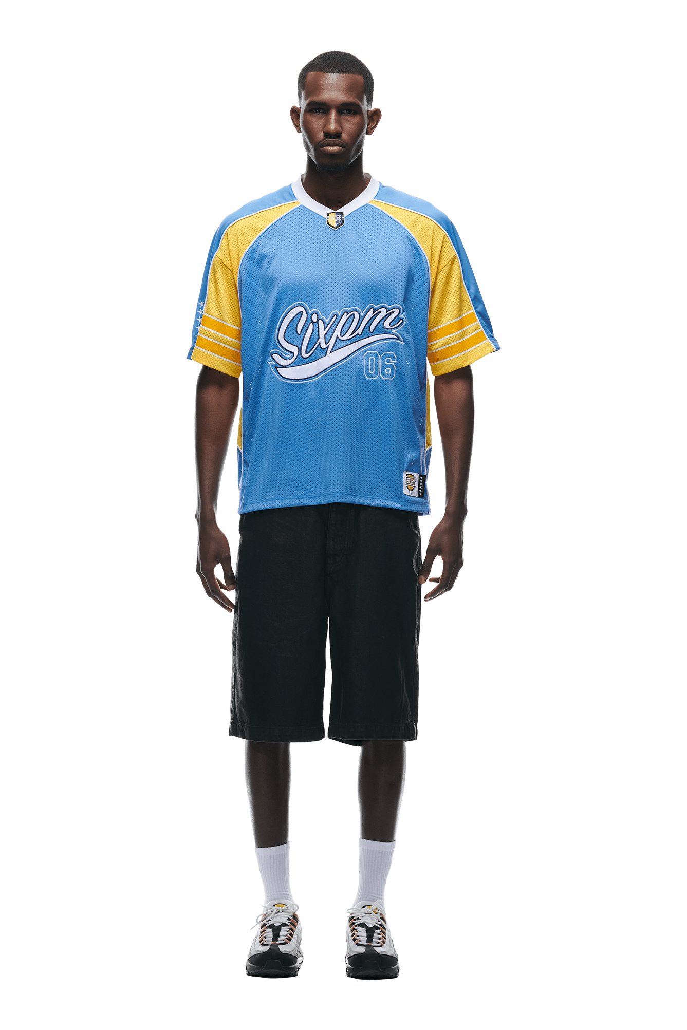 A man faces forward against a white background, wearing the SUMMER FOOTBALL JERSEY BLUE by 6PM, black knee-length shorts, white socks, and sneakers.
