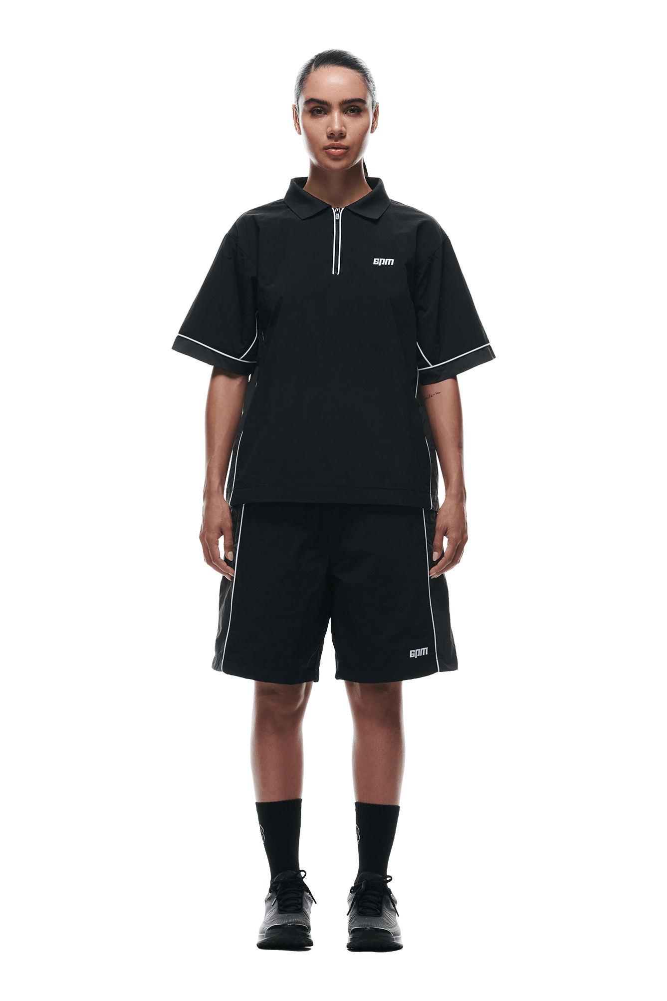 A person faces forward against a white background, wearing the 6PM WARM UP NYLON HALF ZIP BLACK with matching shorts, black socks, and black sneakers.