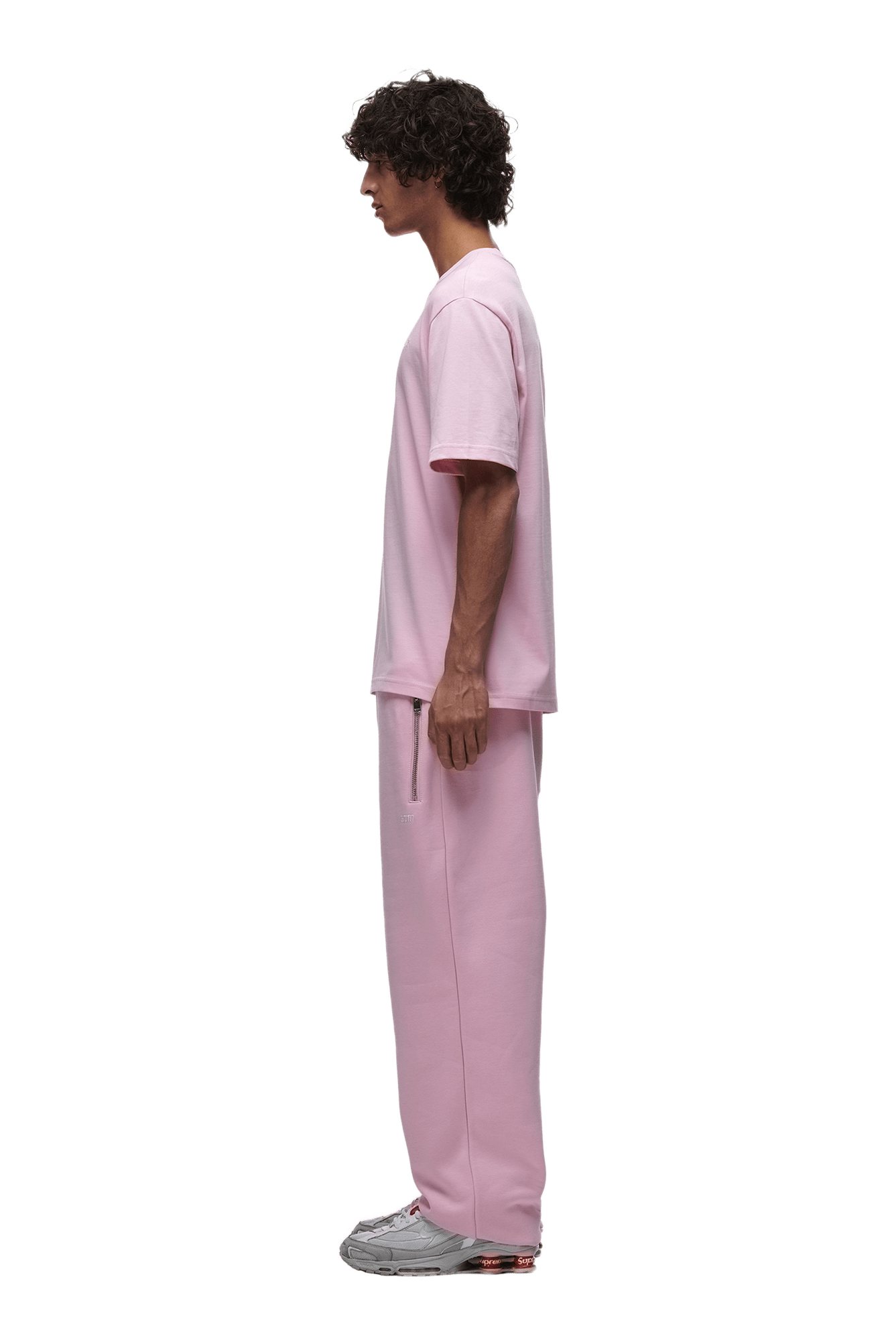 A man in profile wears the 6PM T-SHIRT BABY PINK with matching pink sweatpants and gray sneakers, shown on a transparent background.