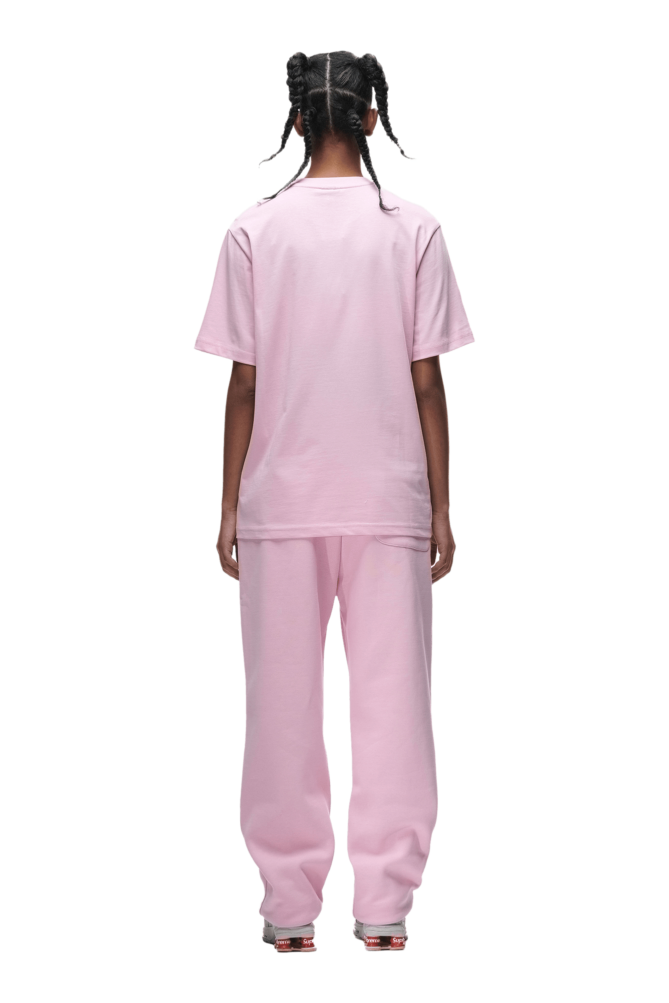 A person with braided hair stands facing away, wearing the 6PM T-SHIRT BABY PINK and matching pink pants with silver shoes. The background is transparent.