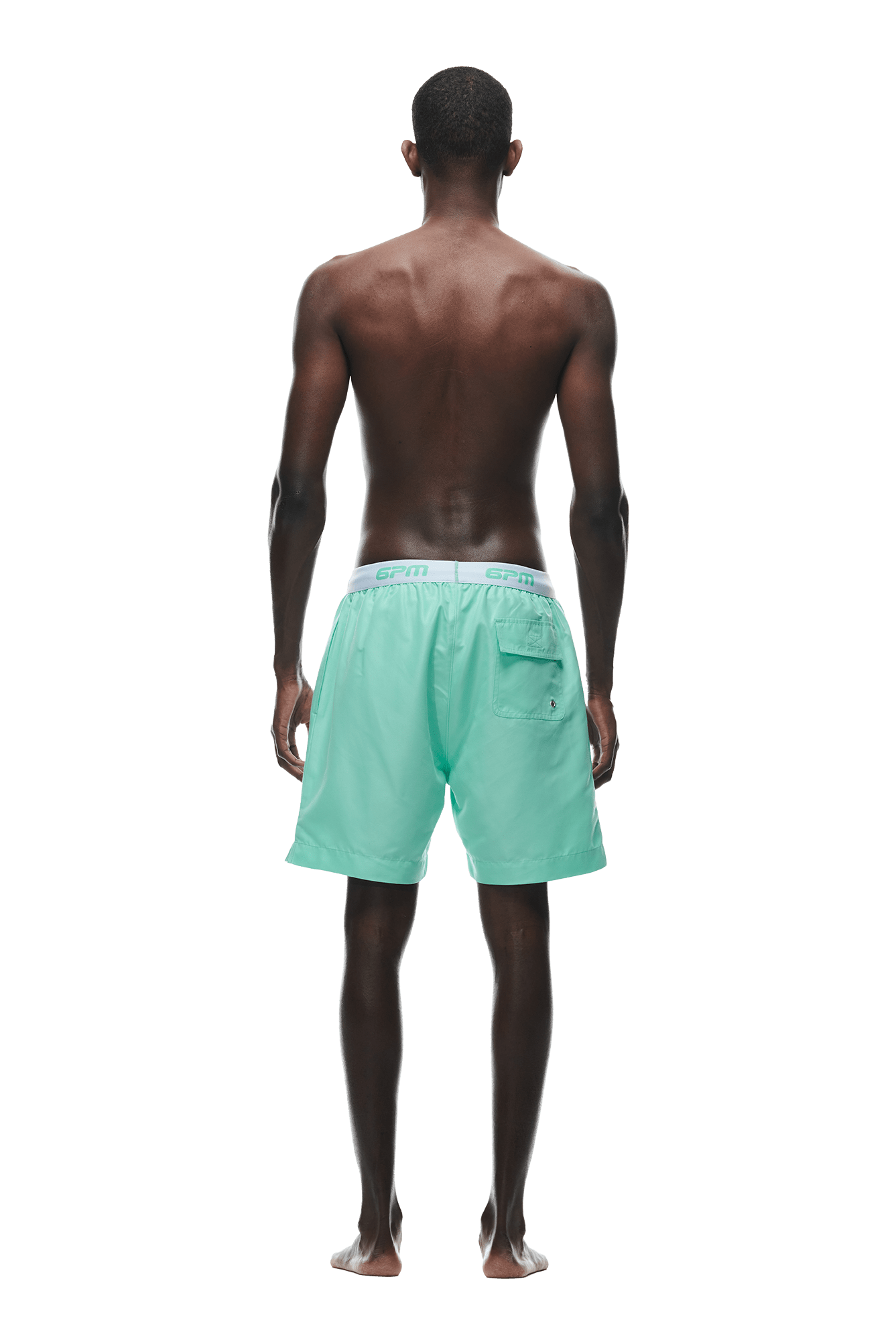 A man stands barefoot with his back to the camera, wearing 6PM BOXER SWIM SHORTS LIGHT MOSS featuring an elastic waistband and back pocket. His upper body is bare, set against a white background.