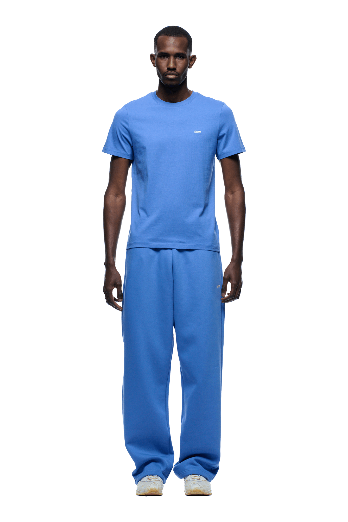A man faces forward in a 6PM SLIM FIT T-SHIRT PERSIAN BLUE and loose sweatpants with white sneakers. The background is transparent.