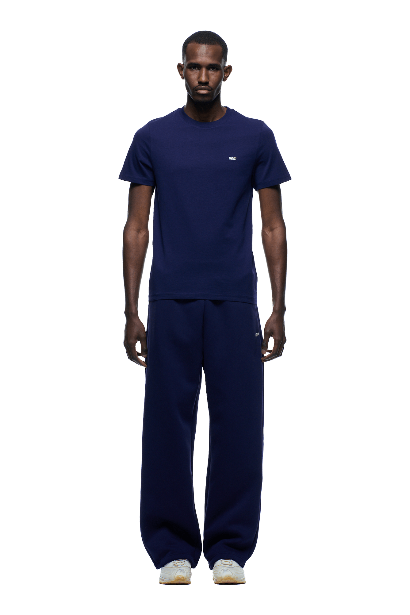 A man stands facing forward, wearing the 6PM SLIM FIT T-SHIRT ORBIT BLUE with matching loose-fit navy blue pants and white sneakers, against a plain background.