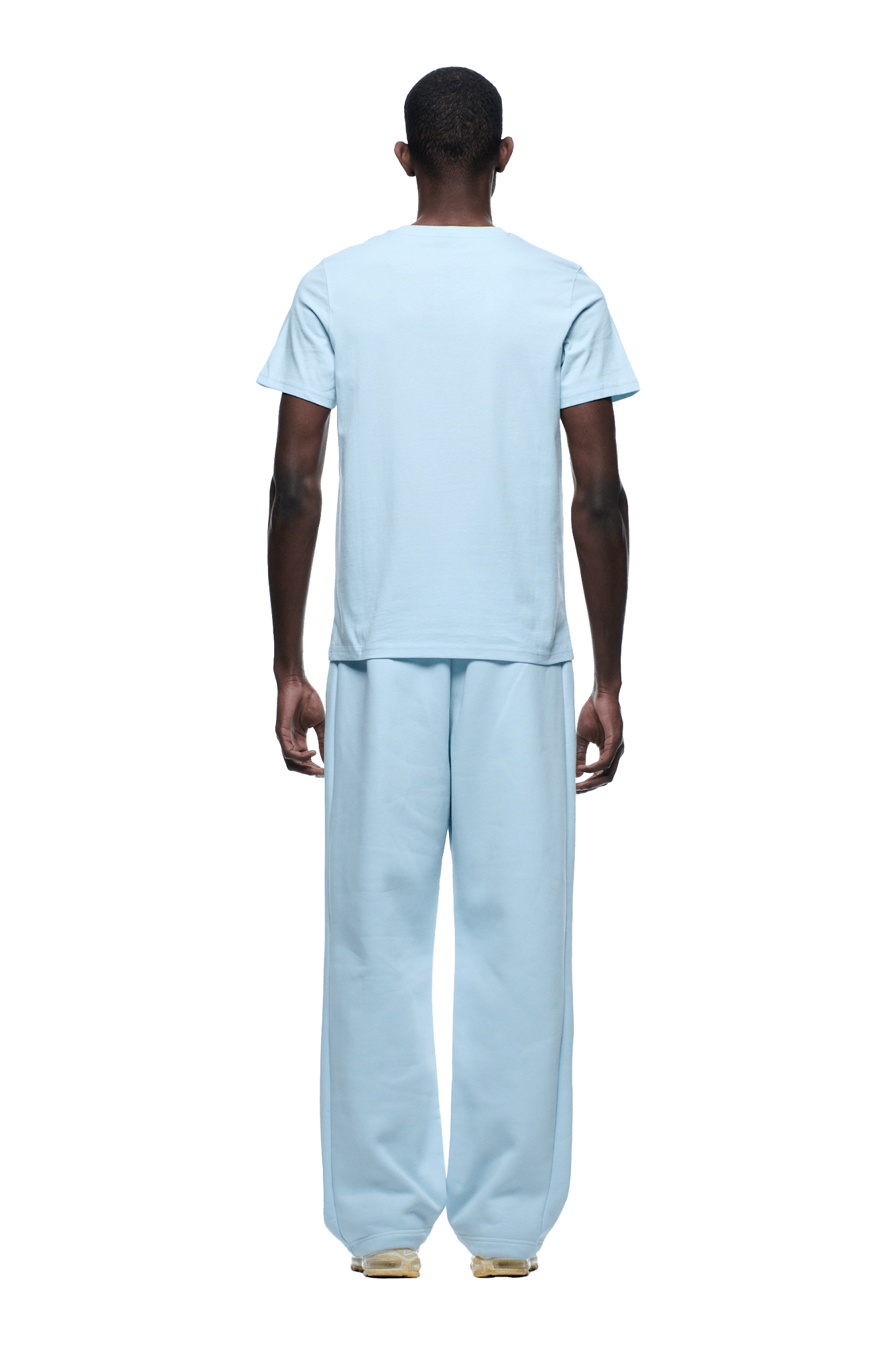 A person, facing away, wears the 6PM SLIM FIT T-SHIRT ICE BLUE (short-sleeve, premium cotton) with loose light blue pants and beige shoes on a transparent background.