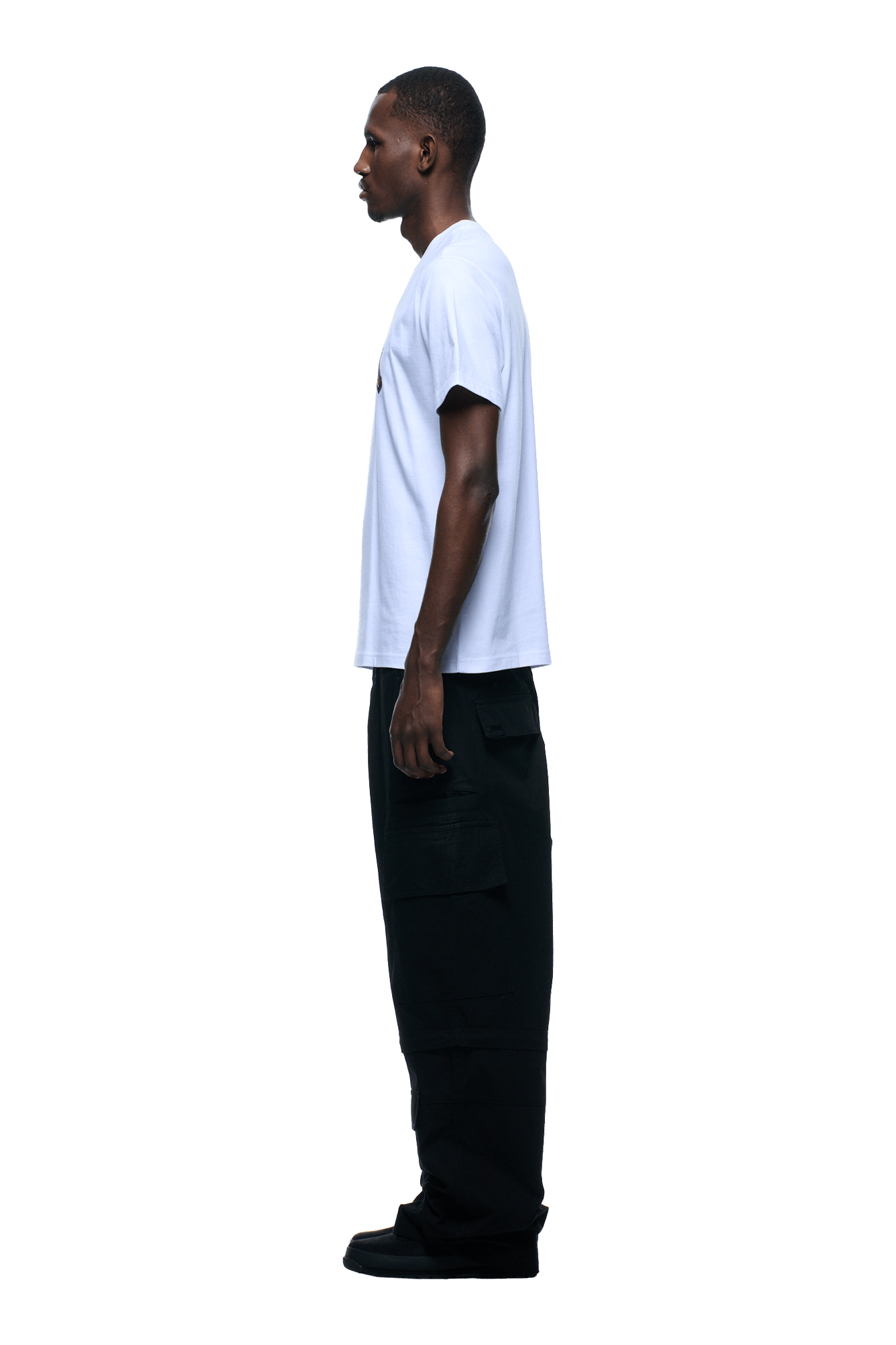 A person in profile faces left, wearing the 6PM OLD ENGLISH CAMO TEE WHITE and black cargo pants with black shoes, set against a plain, transparent background.