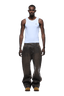A man faces forward against a plain green background, wearing a fitted white tank top, 6PM WAX COATED DENIM BROWN jeans, and tan shoes.