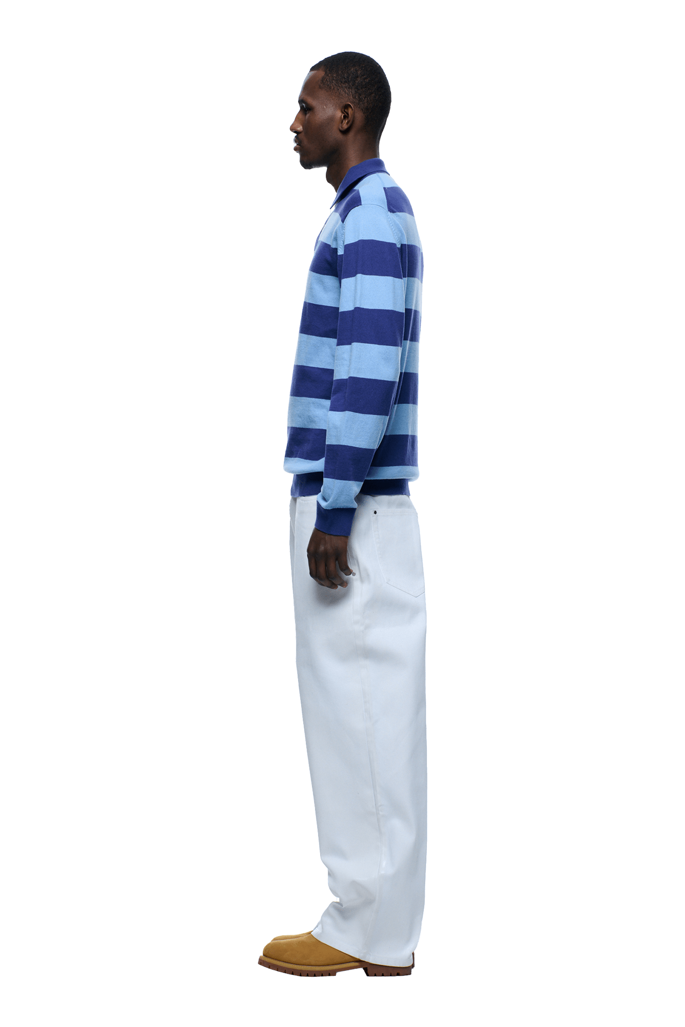 A man stands in profile against a plain background, wearing the 6PM LS STRIPED POLO BLUE with loose white pants and tan shoes.