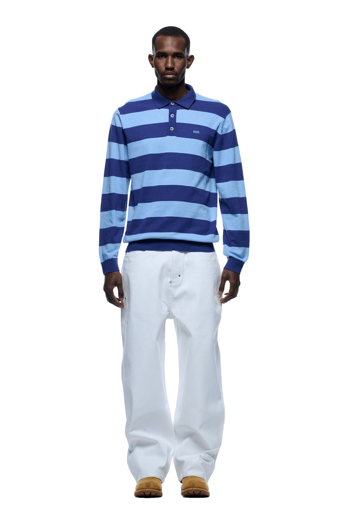 A man stands facing forward, wearing the 6PM LS STRIPED POLO BLUE with loose white pants and tan shoes against a plain background.