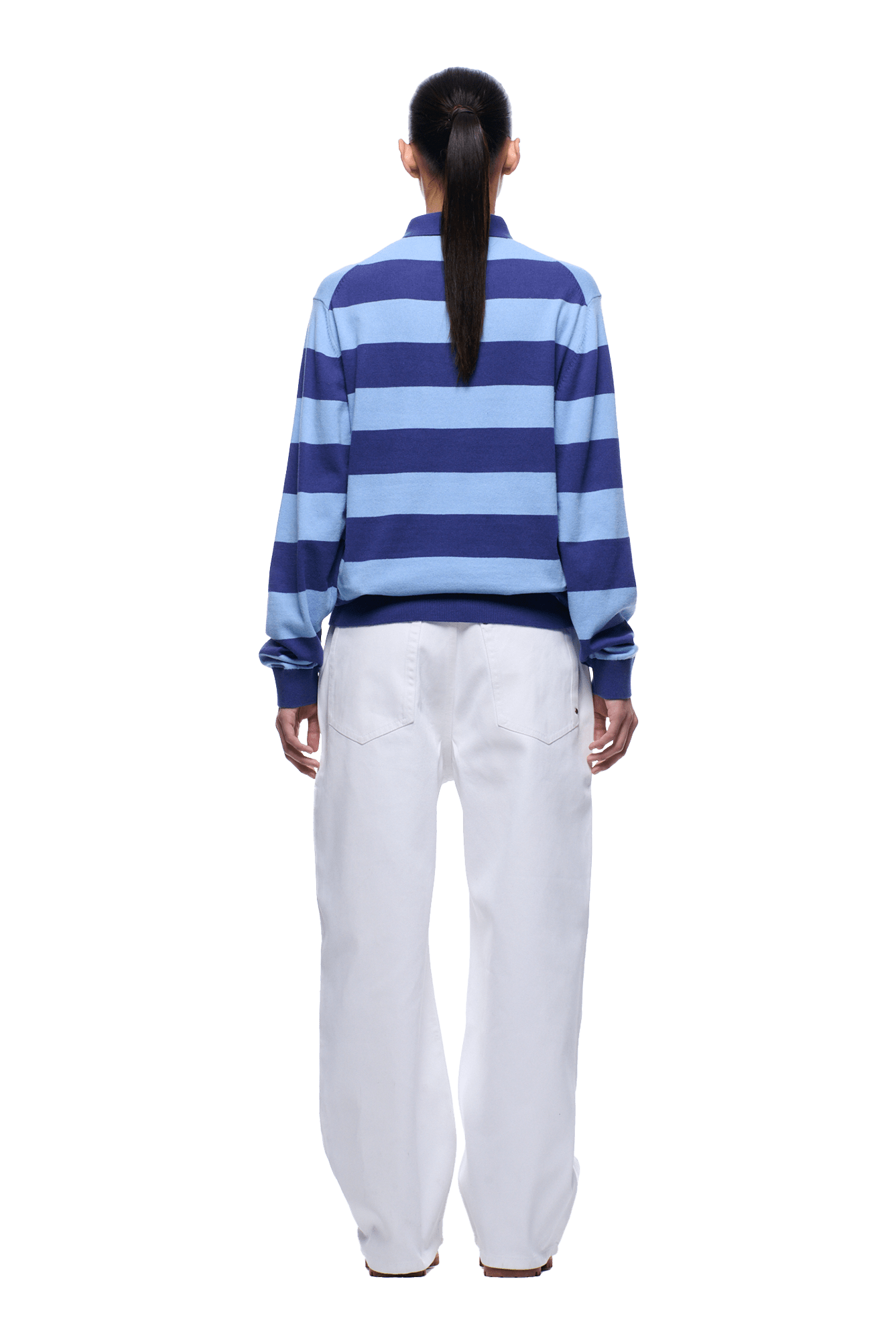 A person stands facing away, wearing the 6PM LS STRIPED POLO BLUE with loose white pants and a low ponytail. The background is transparent.