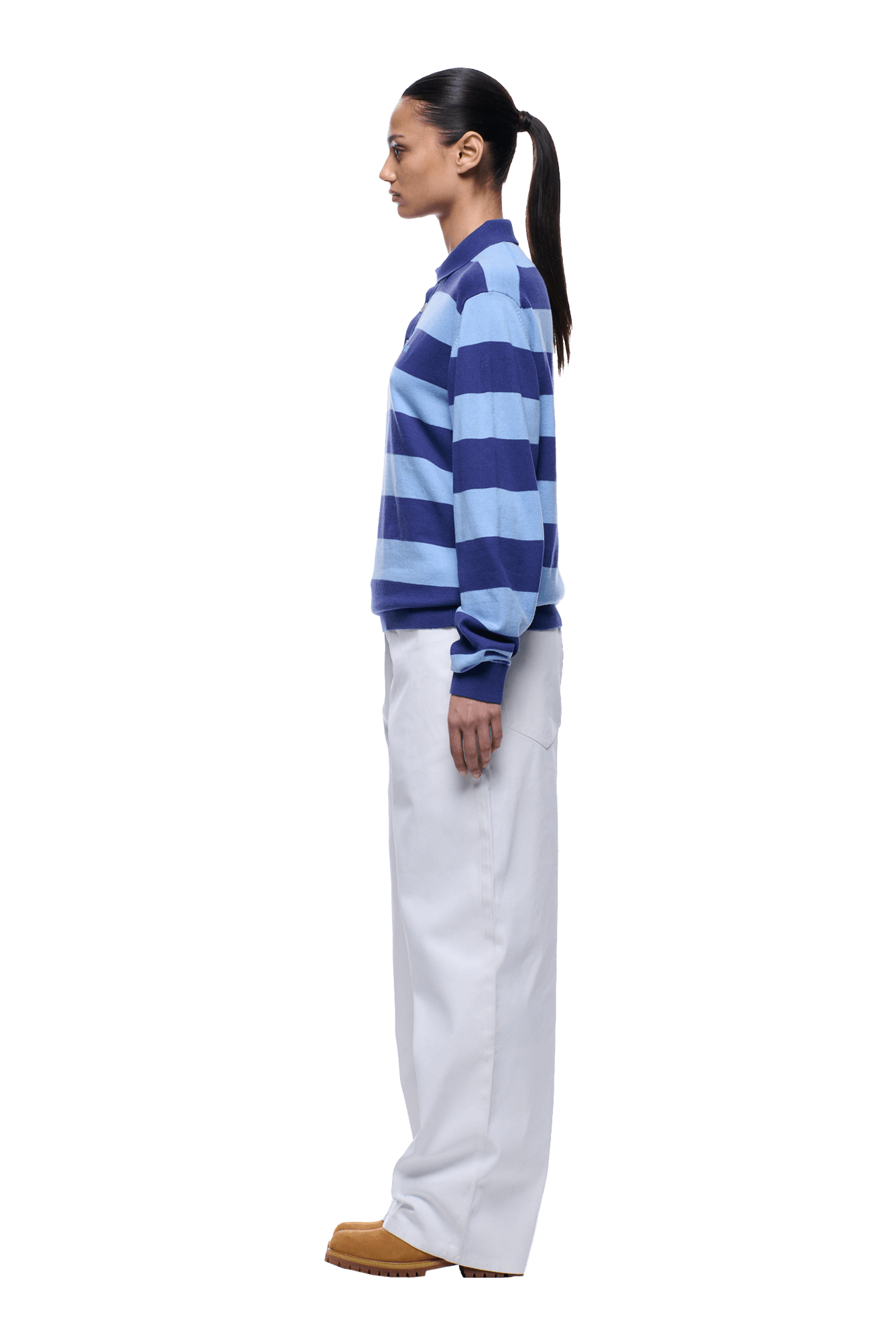 A woman in profile faces left against a transparent background, wearing the 6PM LS STRIPED POLO BLUE sweater, white pants, and brown shoes. Her dark hair is tied back in a ponytail.