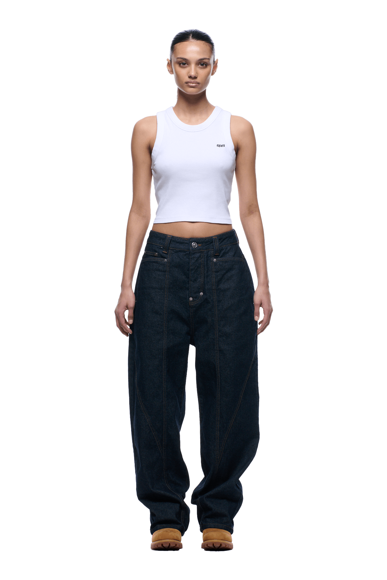 A person stands facing forward, wearing a white sleeveless crop top, 6PM TYPE 6 DENIM BLUE RAW loose-fitting jeans with prominent seams, and tan shoes, against a transparent background.