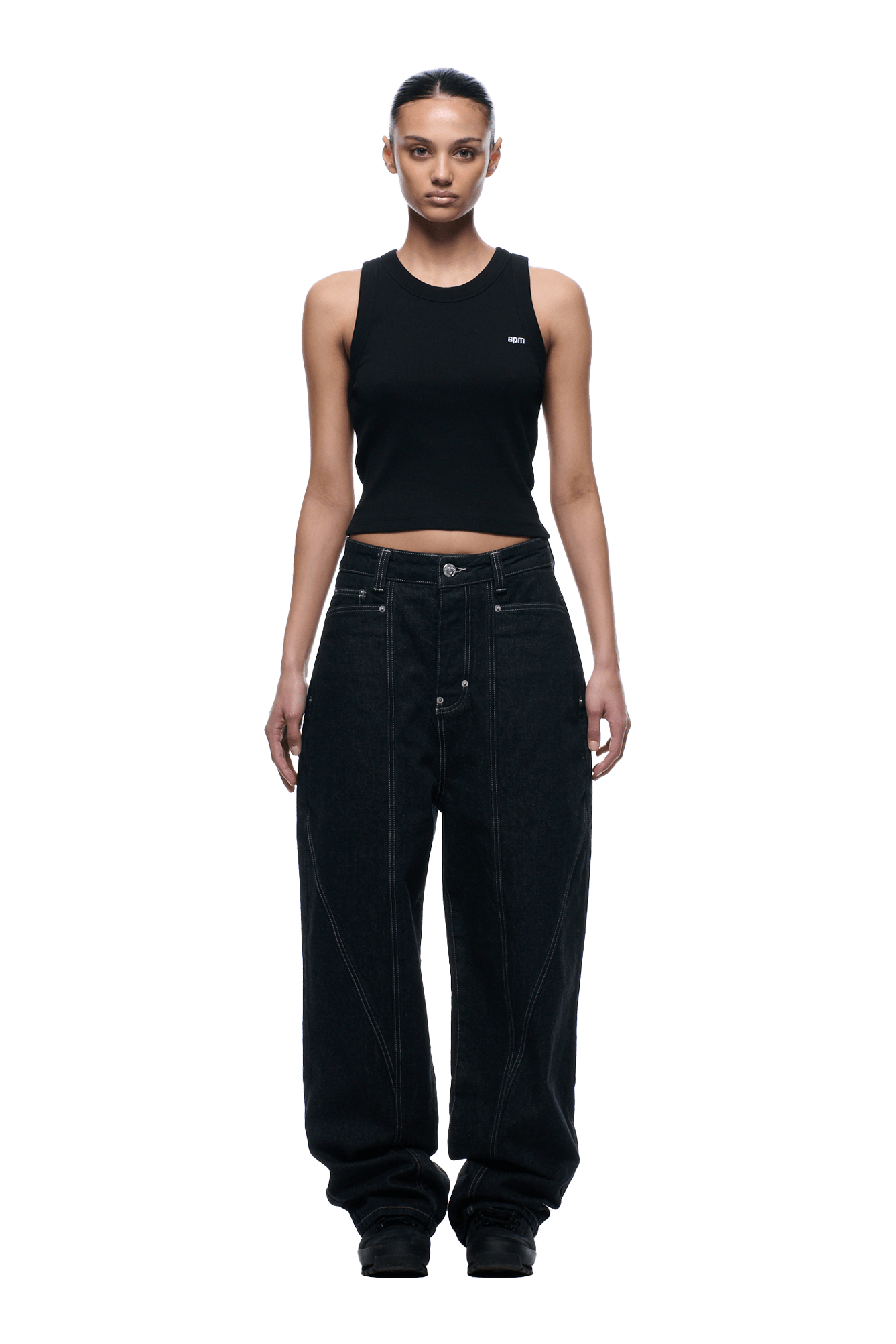 A person stands facing forward against a plain green background, wearing a black sleeveless crop top and 6PM TYPE 6 DENIM BLACK RAW loose-fitting, high-waisted jeans with visible seams. Their hair is pulled back.