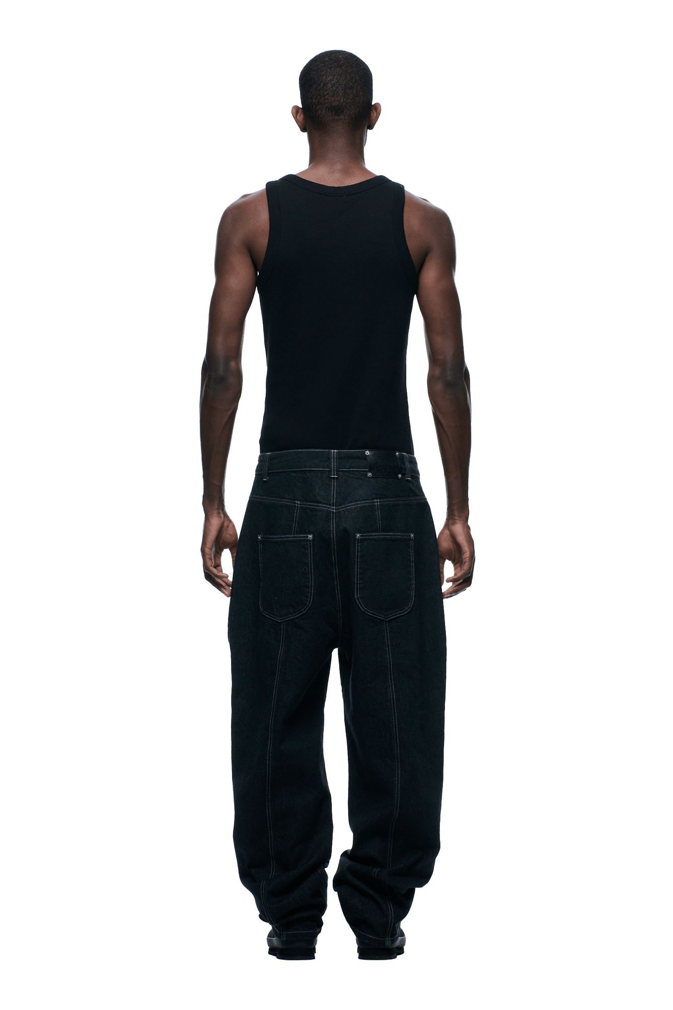 A person stands facing away from the camera, wearing a black tank top and 6PM TYPE 6 DENIM BLACK RAW jeans with large back pockets, against a plain background.