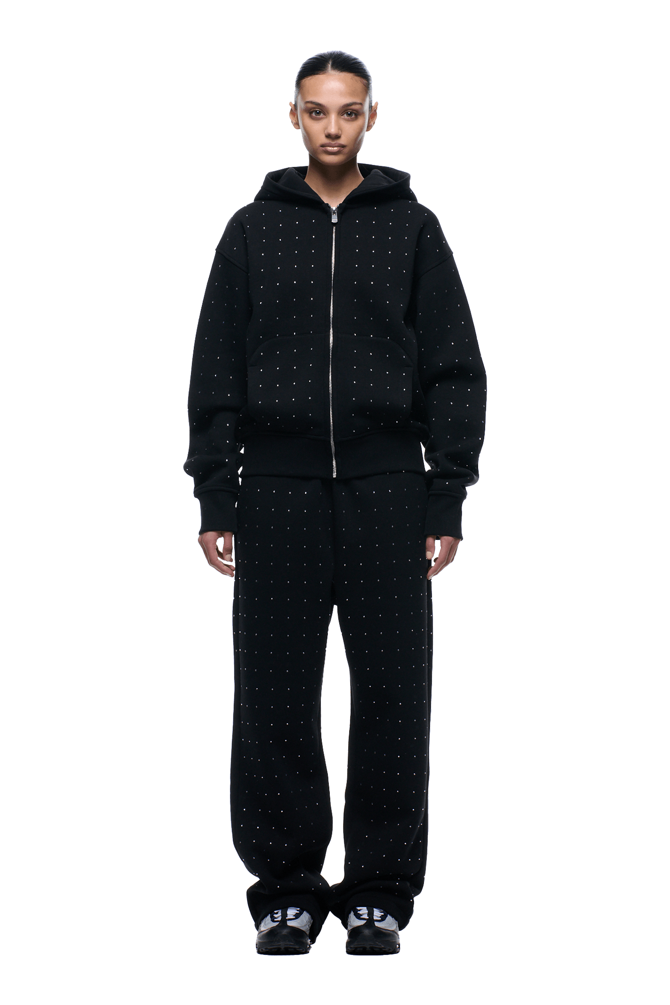 A person stands facing forward wearing the 6PM RHINESTONE LETTER ZIP HOODIE BLACK and matching black sweatpants with small white dot patterns, plus black sneakers. The background is transparent.