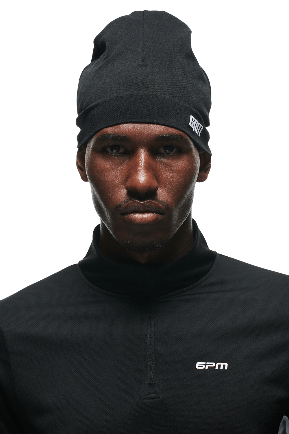 A man wearing the 6PM TECHNICAL LOGO BEANIE and a black zip-up top with 6PM branding looks seriously at the camera against a plain background.