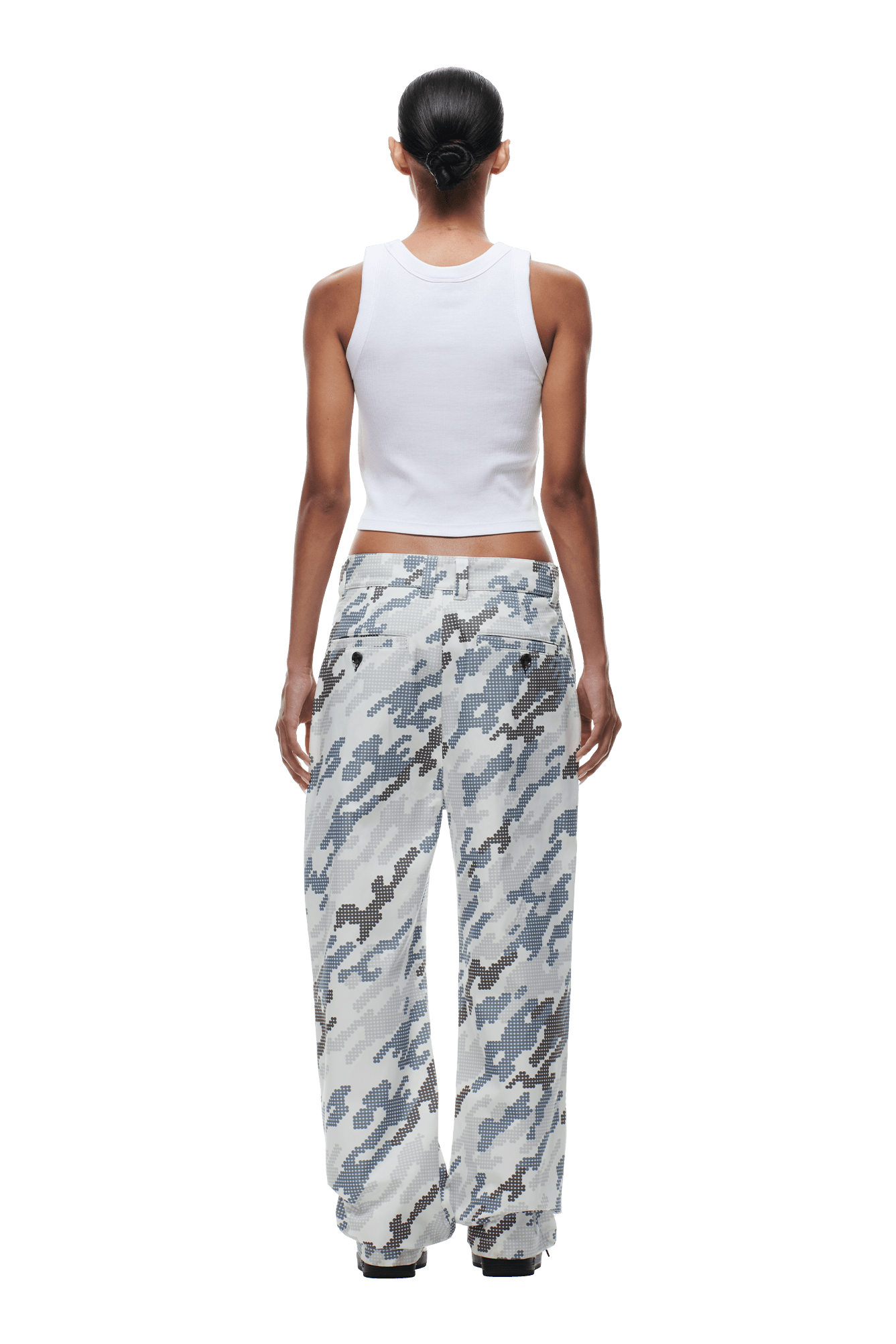 A person with dark hair in a low bun, wearing a white sleeveless crop top and 6PM DOT CAMO CHINO PANTS in light gray and blue, stands facing away from the camera against a transparent background.