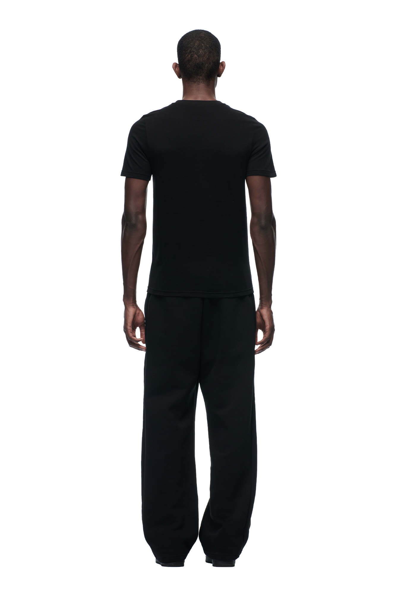 A person stands with their back to the camera, wearing the 6PM SLIM FIT T-SHIRT BLACK and loose black pants against a white background.