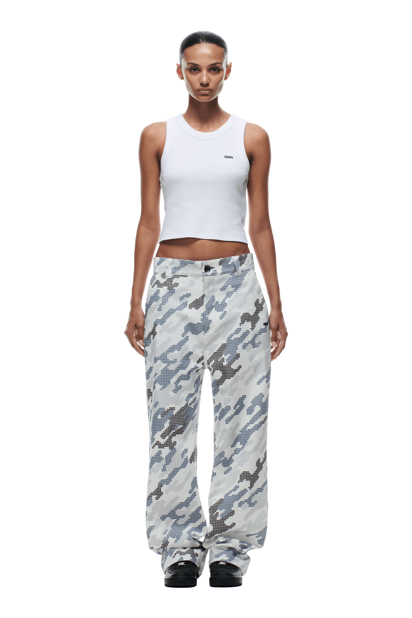 A woman wearing a fitted white sleeveless crop top, 6PM DOT CAMO CHINO PANTS in light gray camouflage, and black shoes stands against a transparent background.