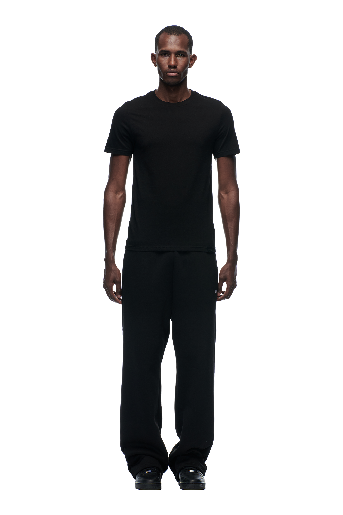 A man faces forward against a plain white background, wearing the 6PM SLIM FIT T-SHIRT BLACK, paired with black pants and black shoes.