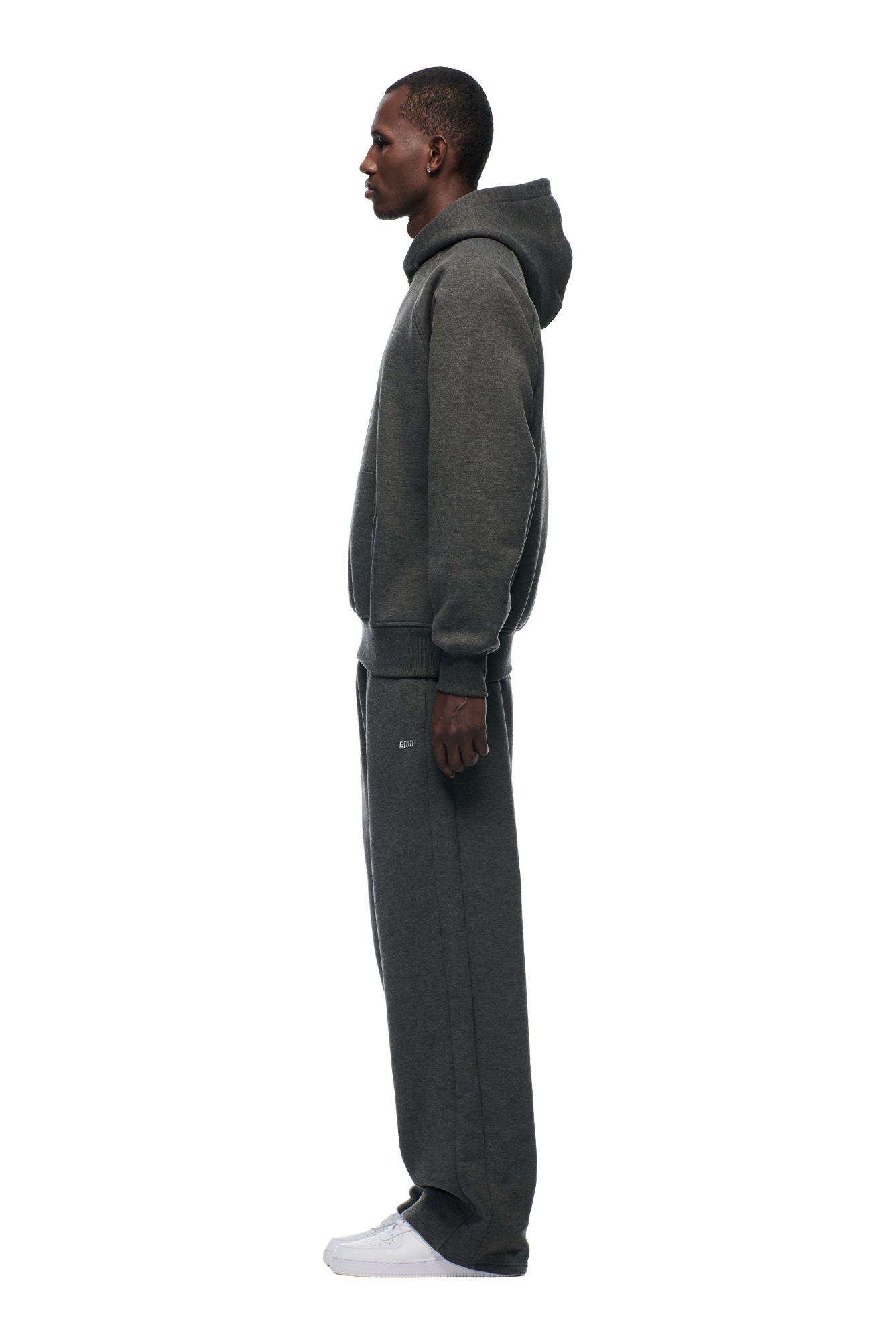 A man in profile wears the 6PM HOODIE DARK GREY MELANGE with matching sweatpants and white sneakers, standing against a plain white background.