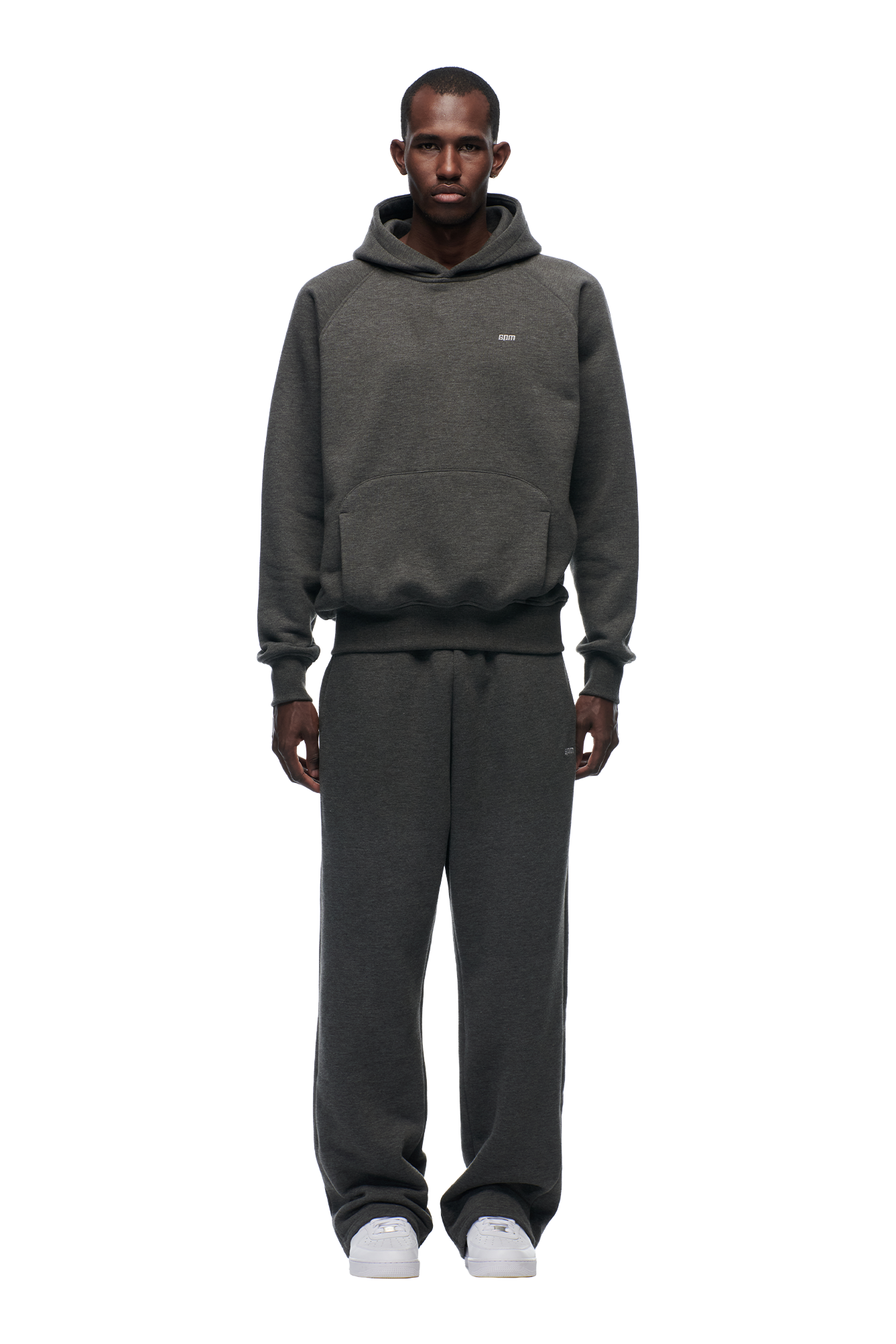 A man stands facing forward against a white background, wearing the 6PM HOODIE DARK GREY MELANGE and matching sweatpants with white sneakers.