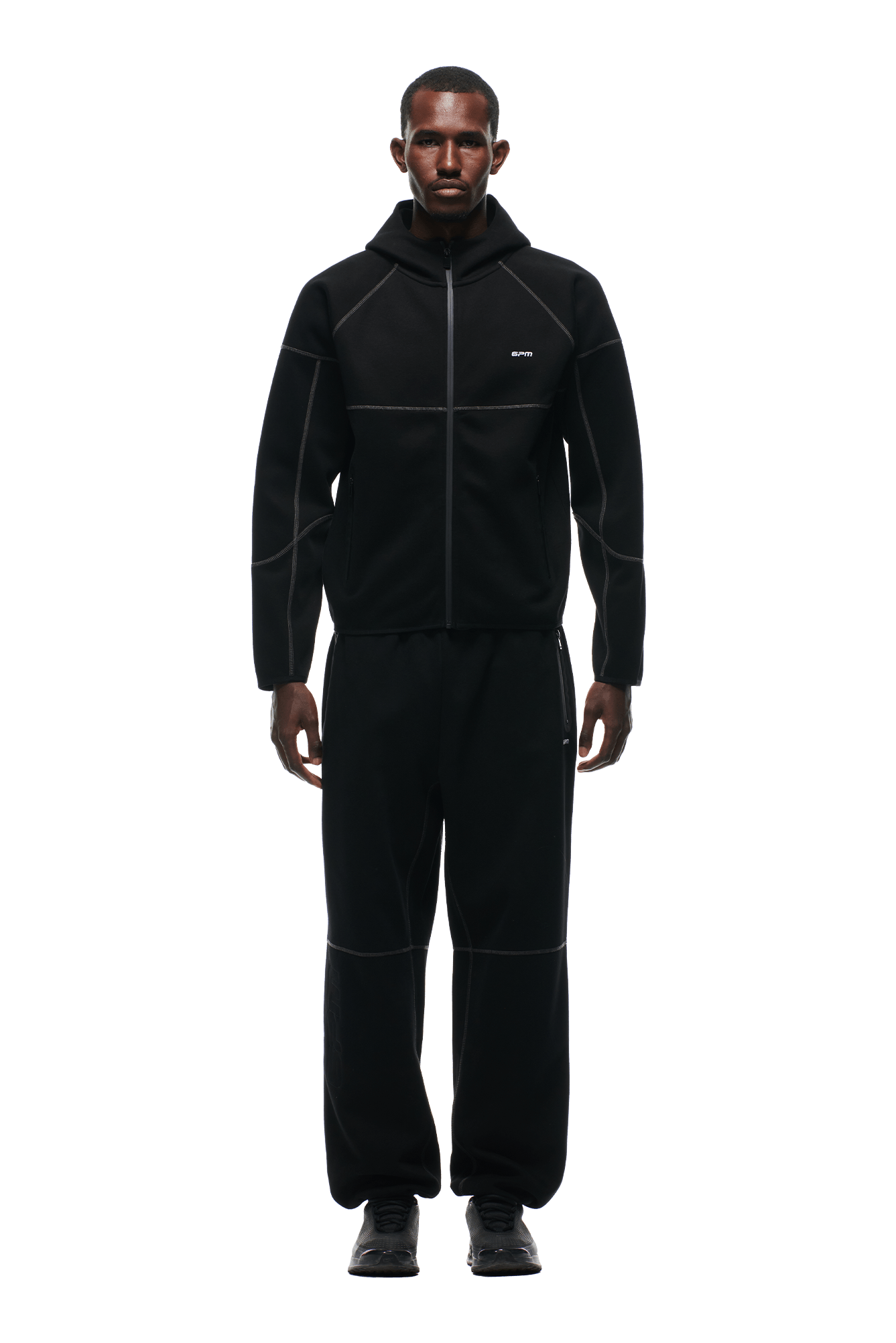 A man faces forward in a 6PM HOODED ROADMAN JACKET with matching black pants featuring visible seams, plus black shoes. The background is transparent.
