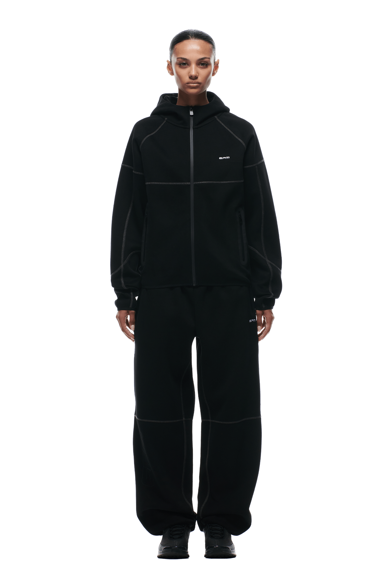 A person faces forward, wearing the 6PM HOODED ROADMAN JACKET—a loose-fitting black zip-up hoodie with minimal white text—paired with matching black pants and black sneakers. The look is sporty and comfortable. The background is transparent.
