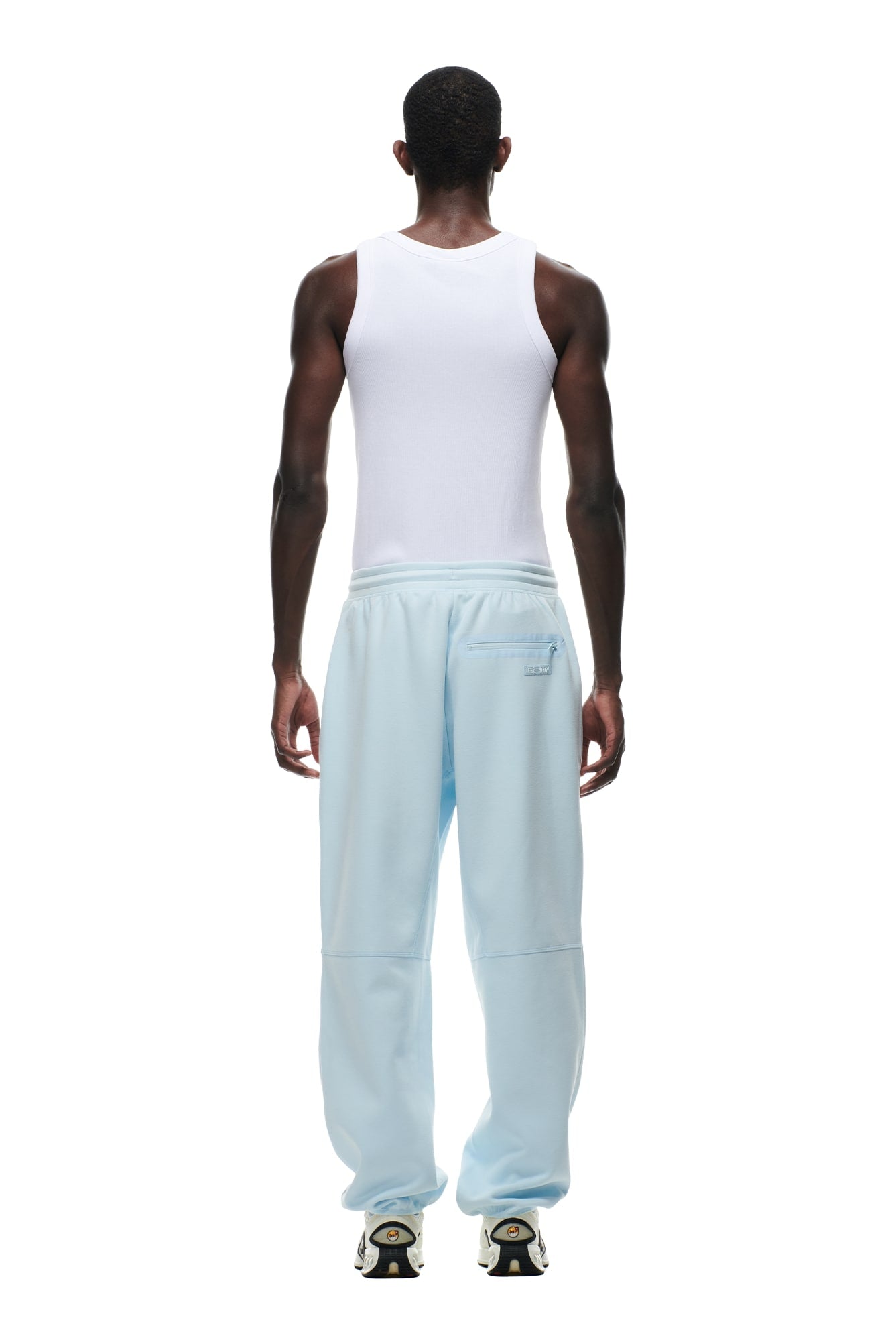 A person faces away wearing 6PM WIDE ROADMAN PANTS in ice blue, featuring patch pockets, paired with a white sleeveless tank top against a plain white background.