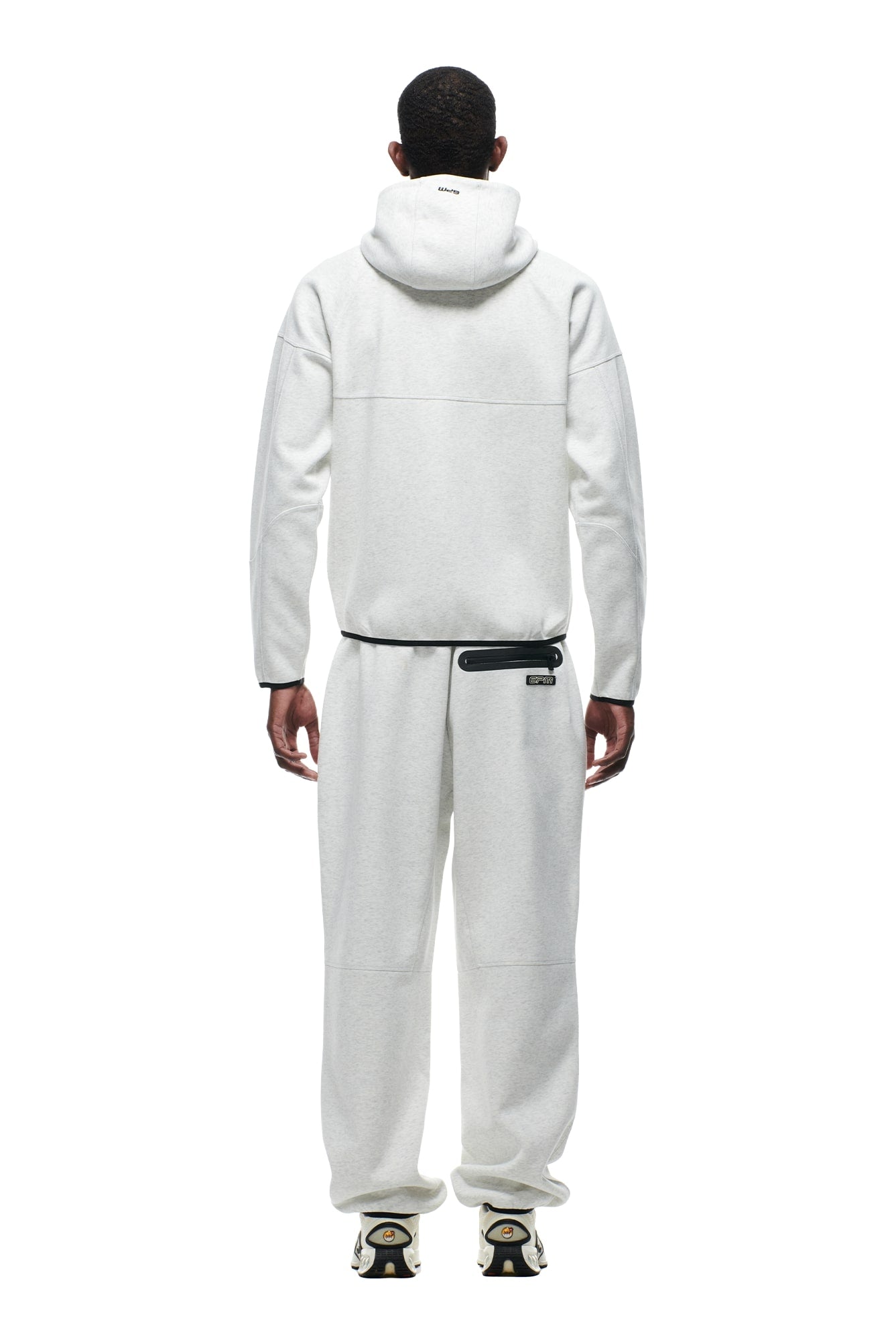 A person faces away wearing the 6PM HOODED ROADMAN JACKET LIGHT GREY, paired with matching sweatpants and white and black sneakers, set against a plain white background.