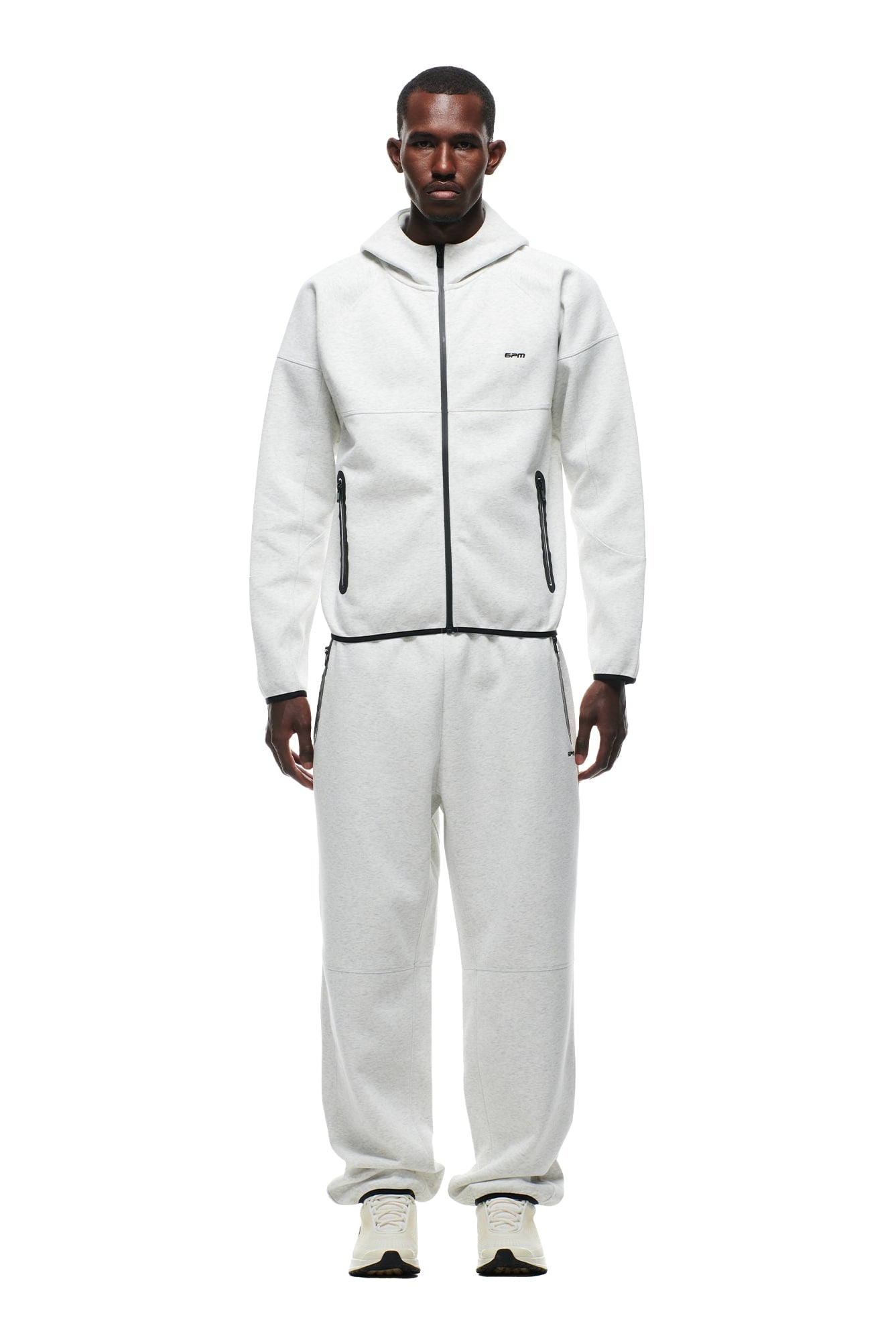 A man faces forward wearing the 6PM HOODED ROADMAN JACKET in light grey, paired with matching sweatpants and white sneakers, set against a plain white background.