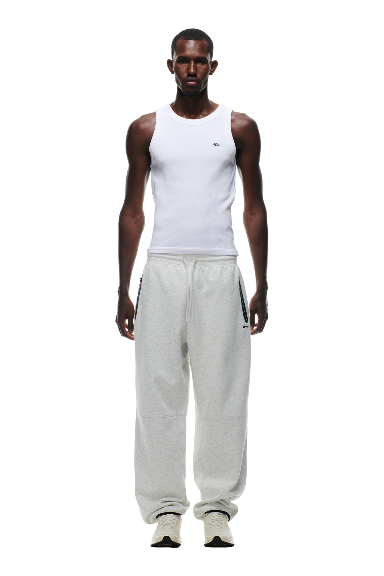 A man faces forward in a white tank top, white sneakers, and 6PM WIDE ROADMAN PANTS in light grey melange, standing against a plain white background.