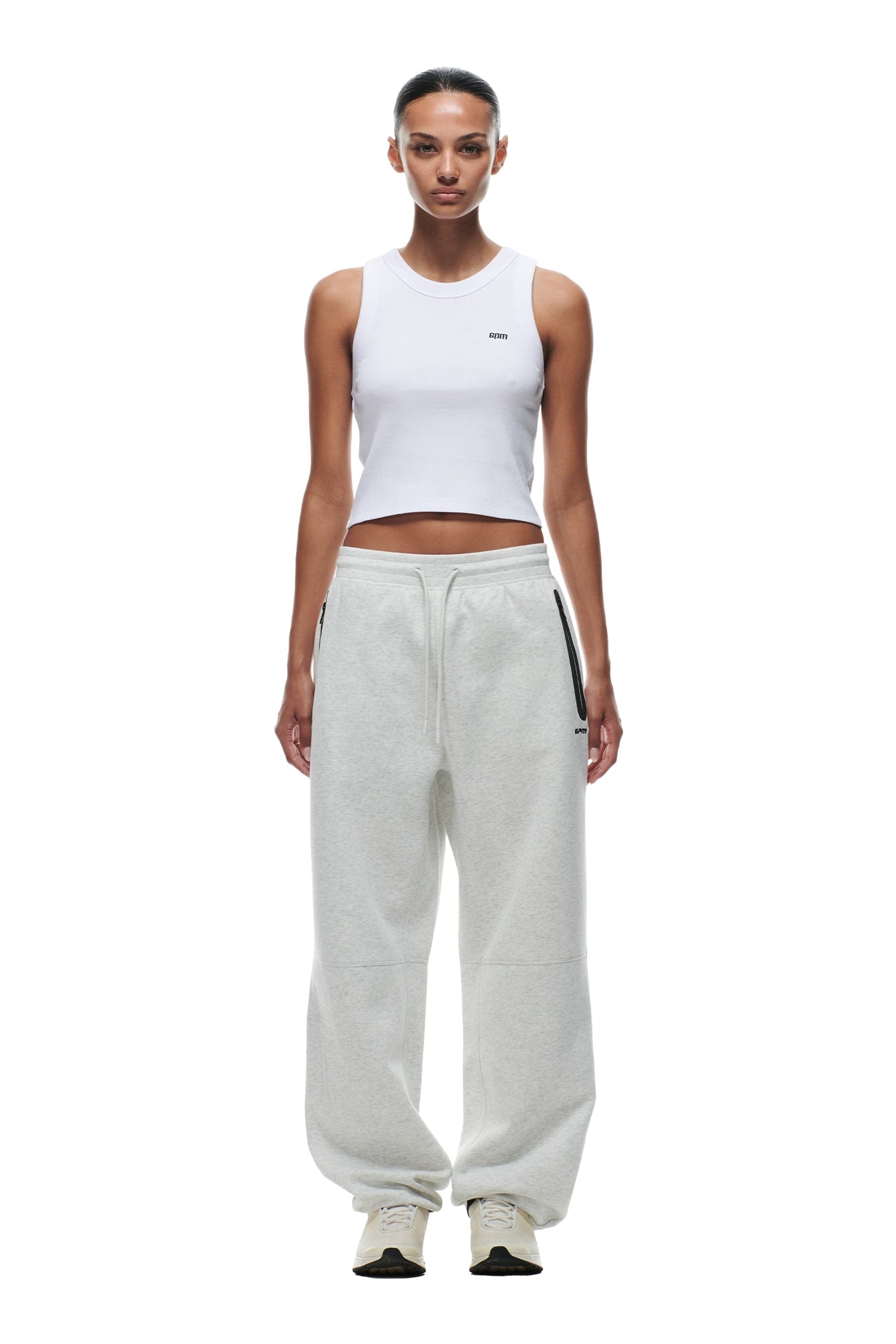 A woman stands facing forward wearing 6PMs WIDE ROADMAN PANTS in Light Grey Melange with a white sleeveless crop top and white sneakers. The background is plain white.