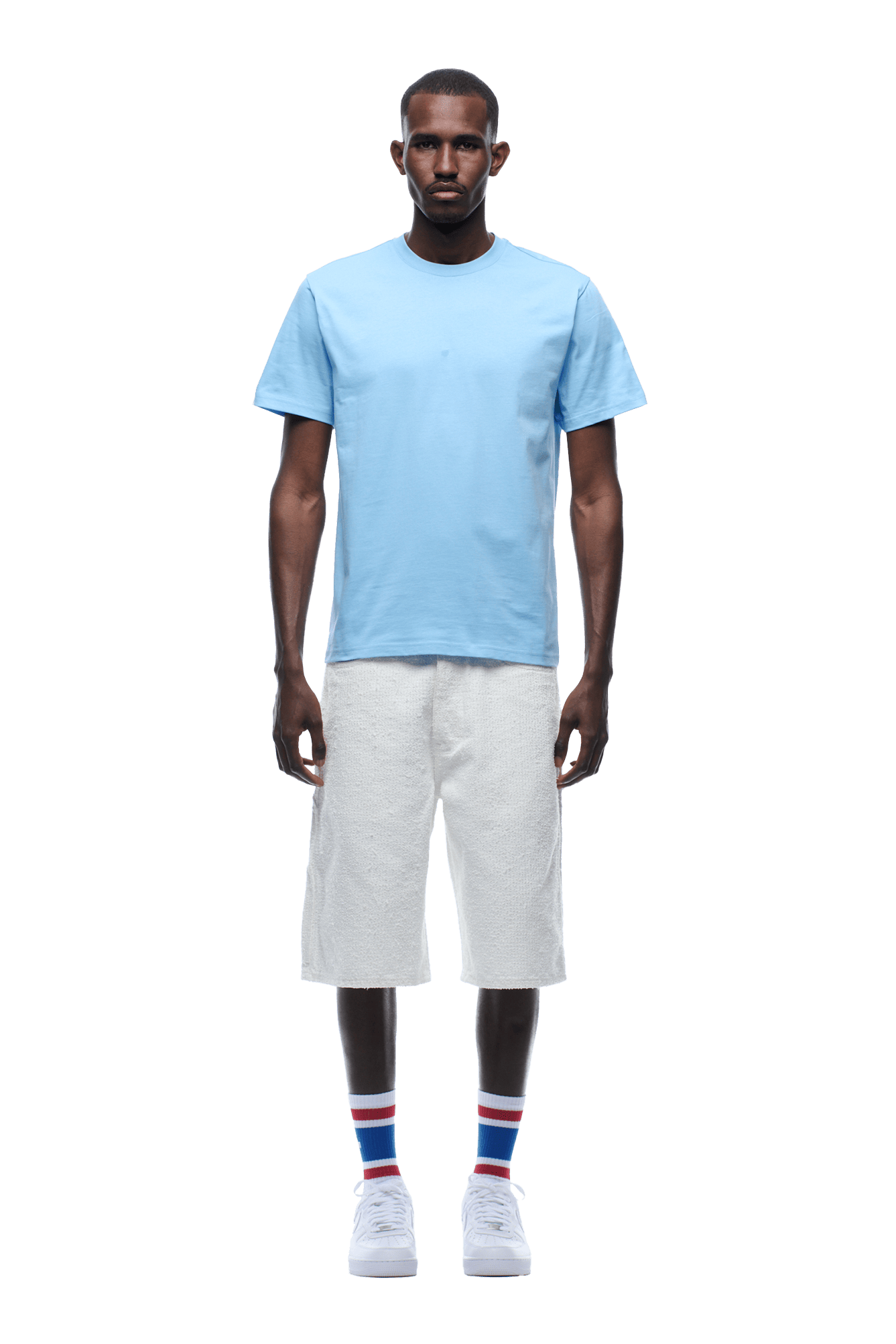 A man stands facing forward, wearing the 6PM COLLEGE STAR TEE BLUE, white knee-length shorts, white sneakers, and white socks with blue and red stripes. The background is transparent.