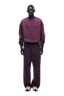 A person stands facing forward, wearing the 6PM CREWNECK PLUM oversized sweatshirt and sweatpants set with white athletic shoes. The background is transparent.
