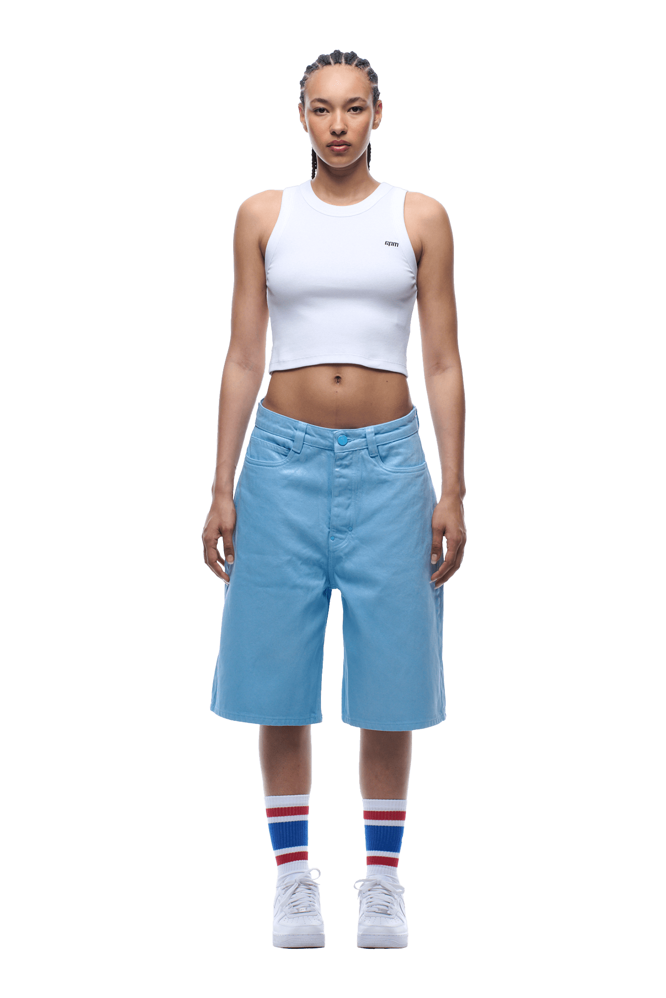 A person stands facing forward, wearing a white cropped tank top, COATED DENIM SHORTS BABY BLUE, white sneakers, and white socks with red and blue stripes. The background is transparent.