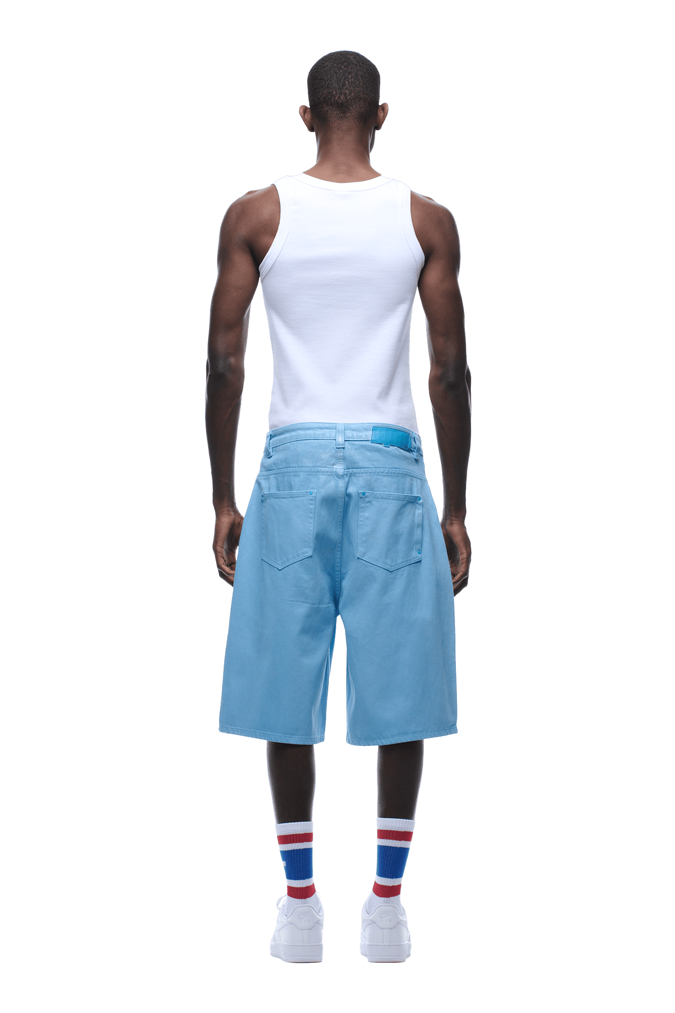 A man faces away, wearing a white sleeveless tank, COATED DENIM SHORTS BABY BLUE, white sneakers, and white socks with red and blue stripes against a plain background.
