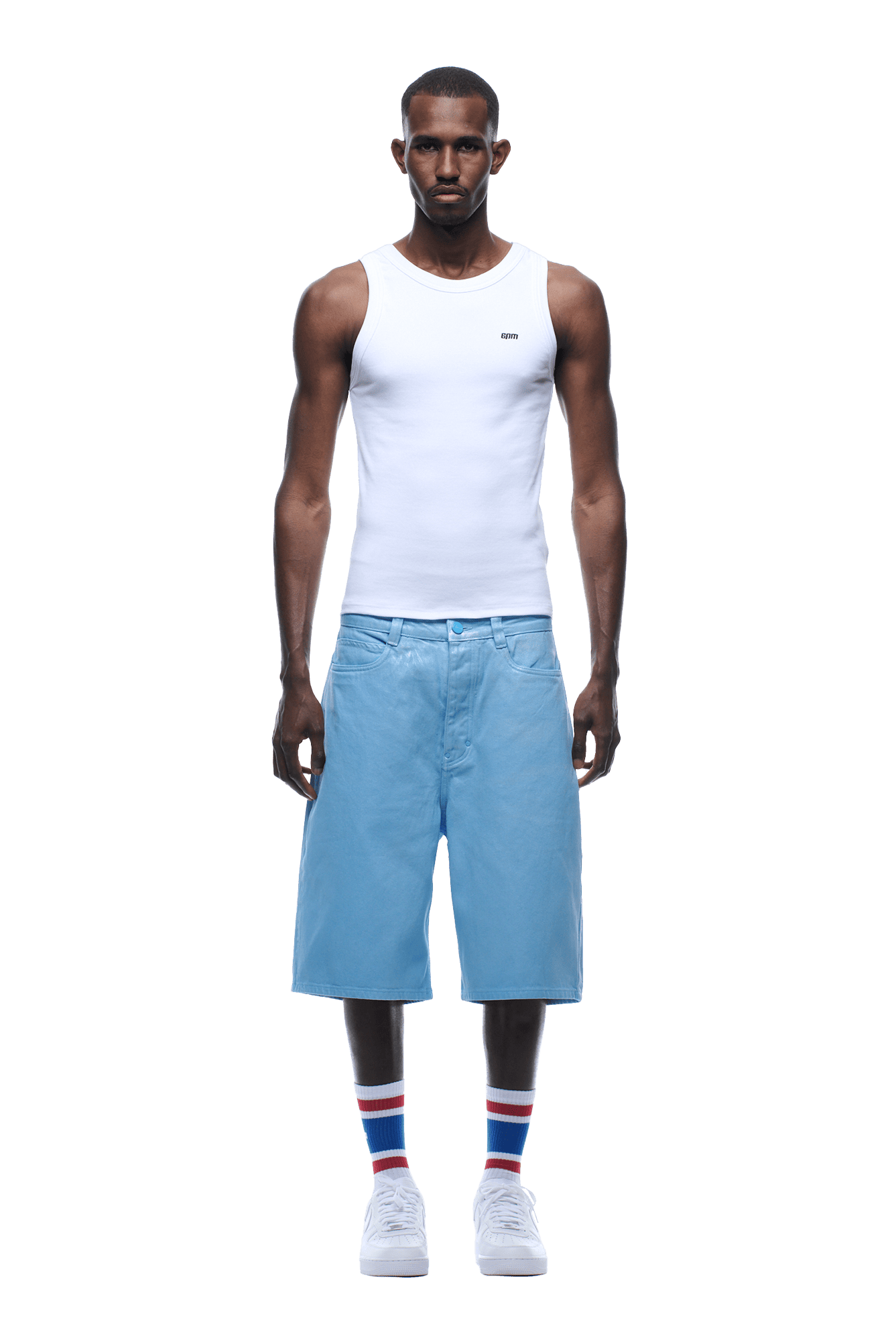 A man stands facing forward, wearing a white tank top, COATED DENIM SHORTS BABY BLUE, white sneakers, and white socks with red and blue stripes on a transparent background.