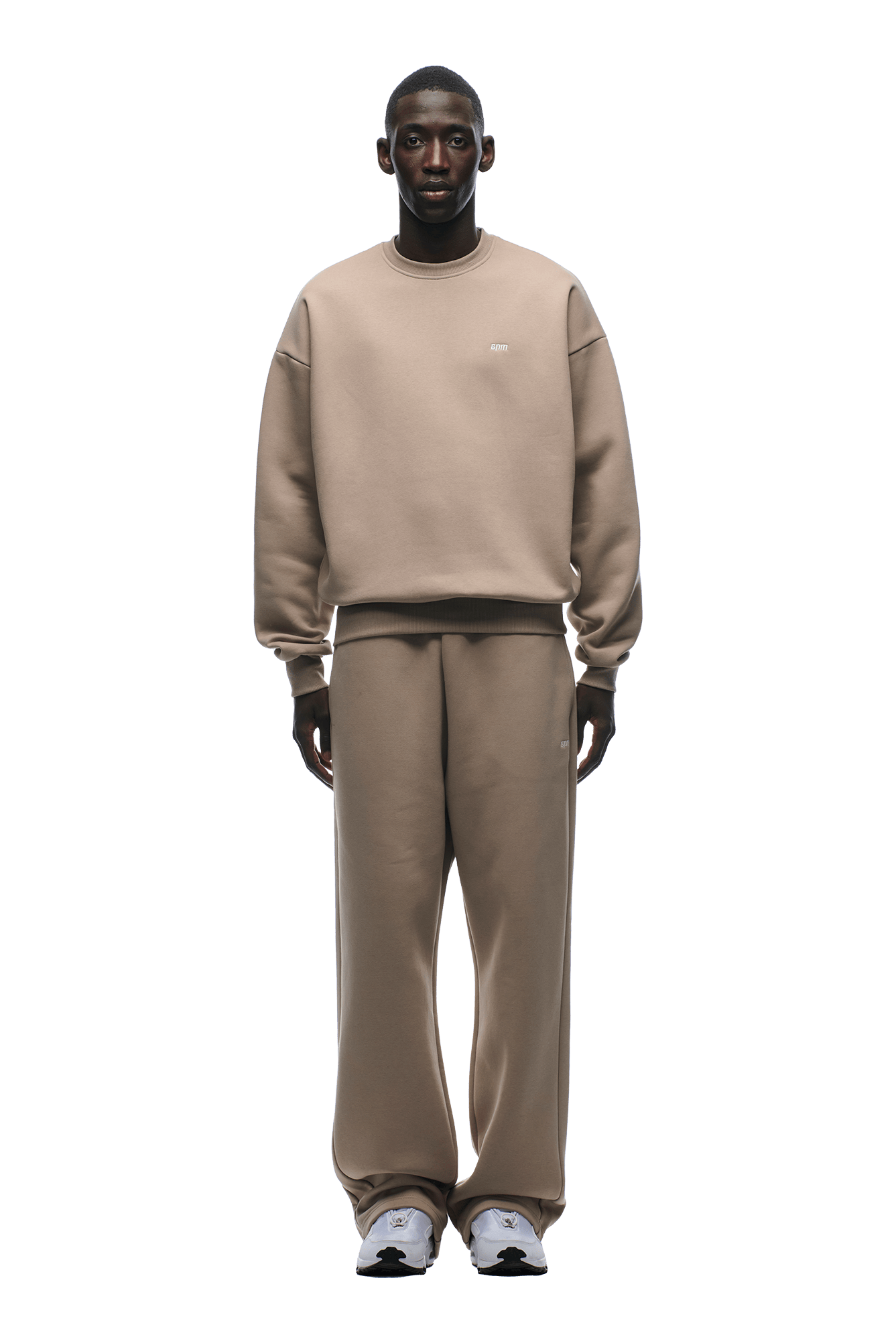 A man faces forward, wearing the 6PM CREWNECK MOCCA CREAM sweatshirt and matching sweatpants with white sneakers, set against a transparent background.