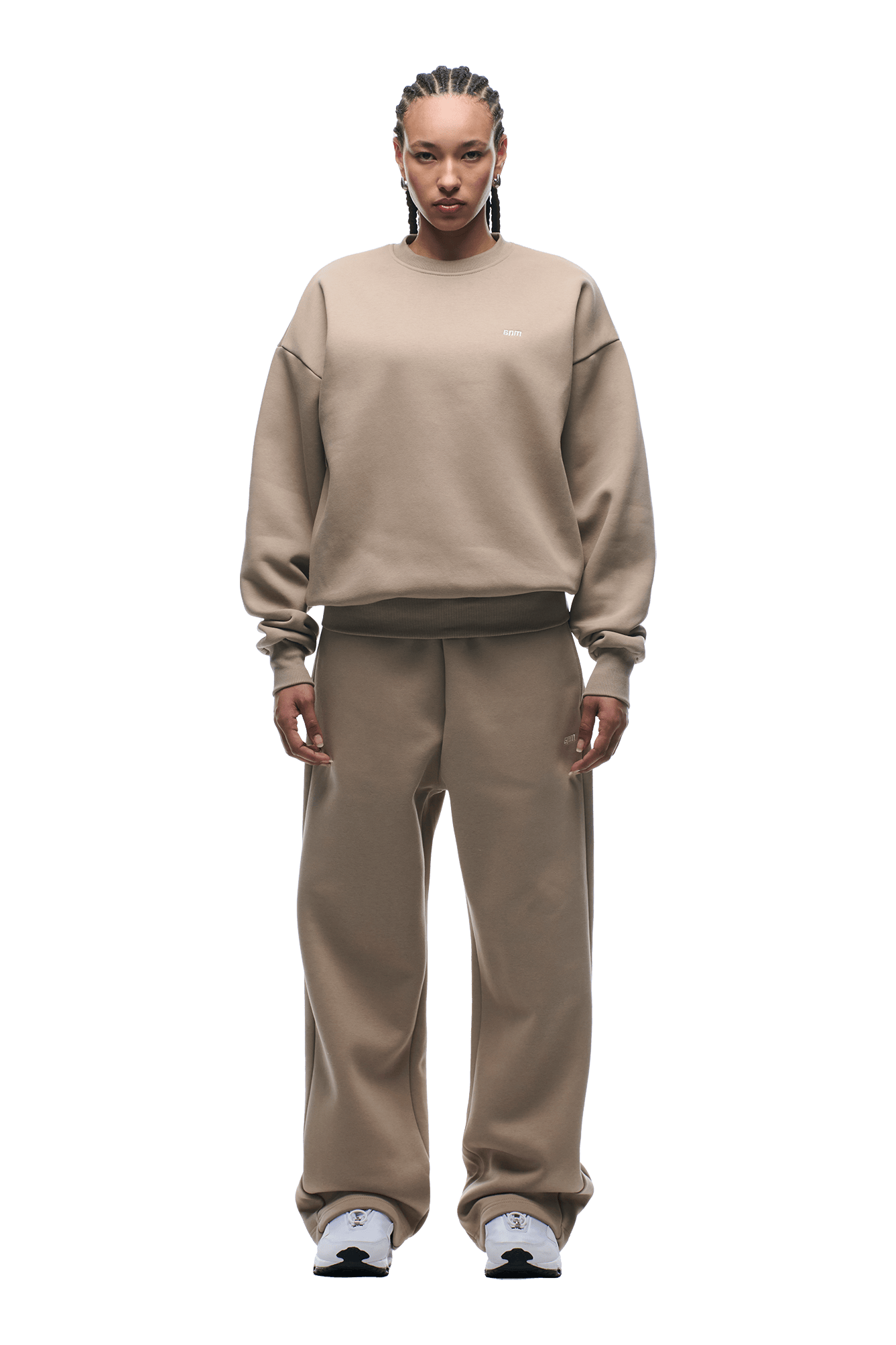 A person with braided hair faces forward, wearing the 6PM CREWNECK MOCCA CREAM sweatshirt and matching pants paired with white sneakers. The fit is boxy, featuring ribbed trims. The background is transparent.