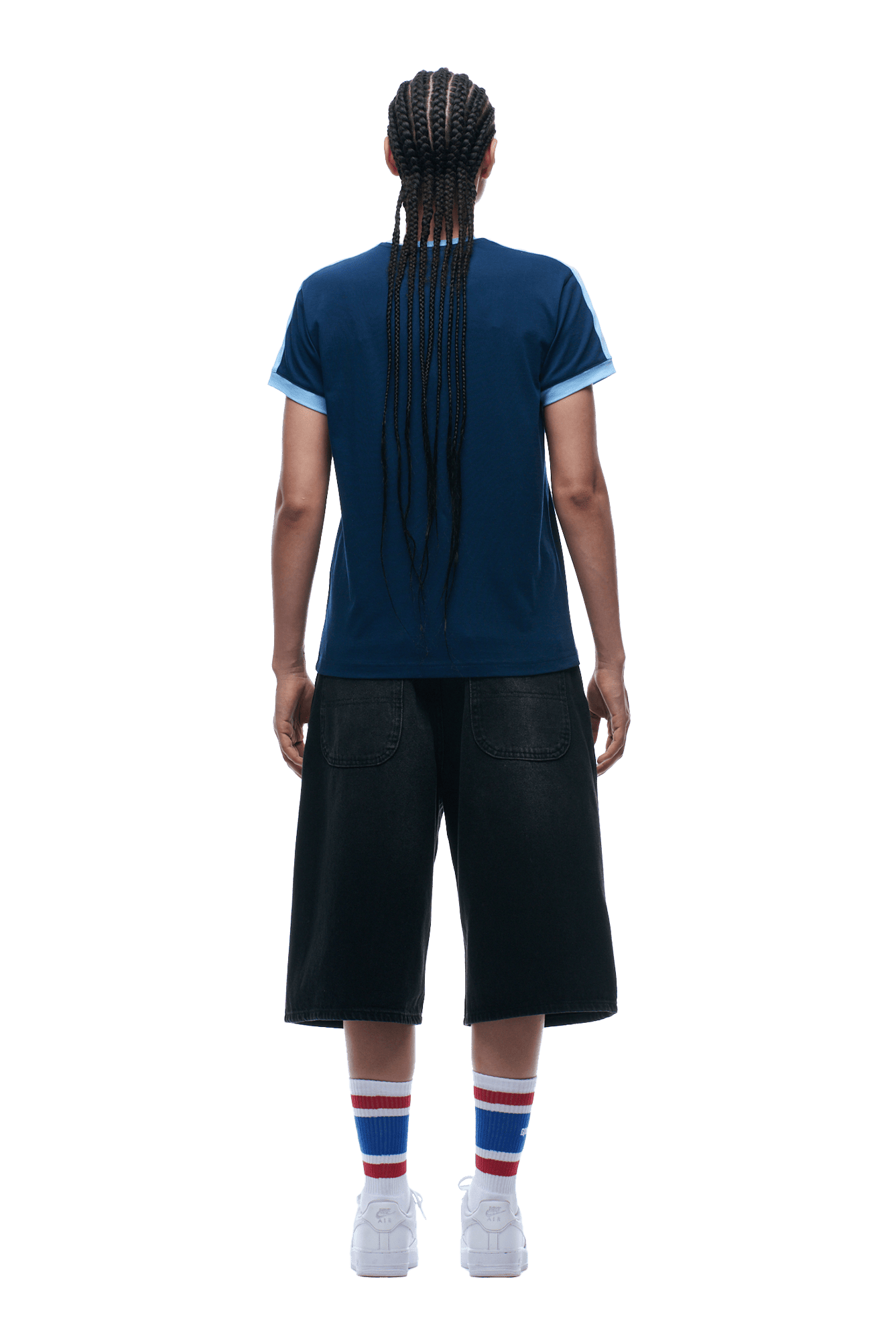 A person with long braided hair faces away, wearing the 6PM SLIM FIT RINGER TEE NAVY, black knee-length shorts, white sneakers, and white socks with red and blue stripes.